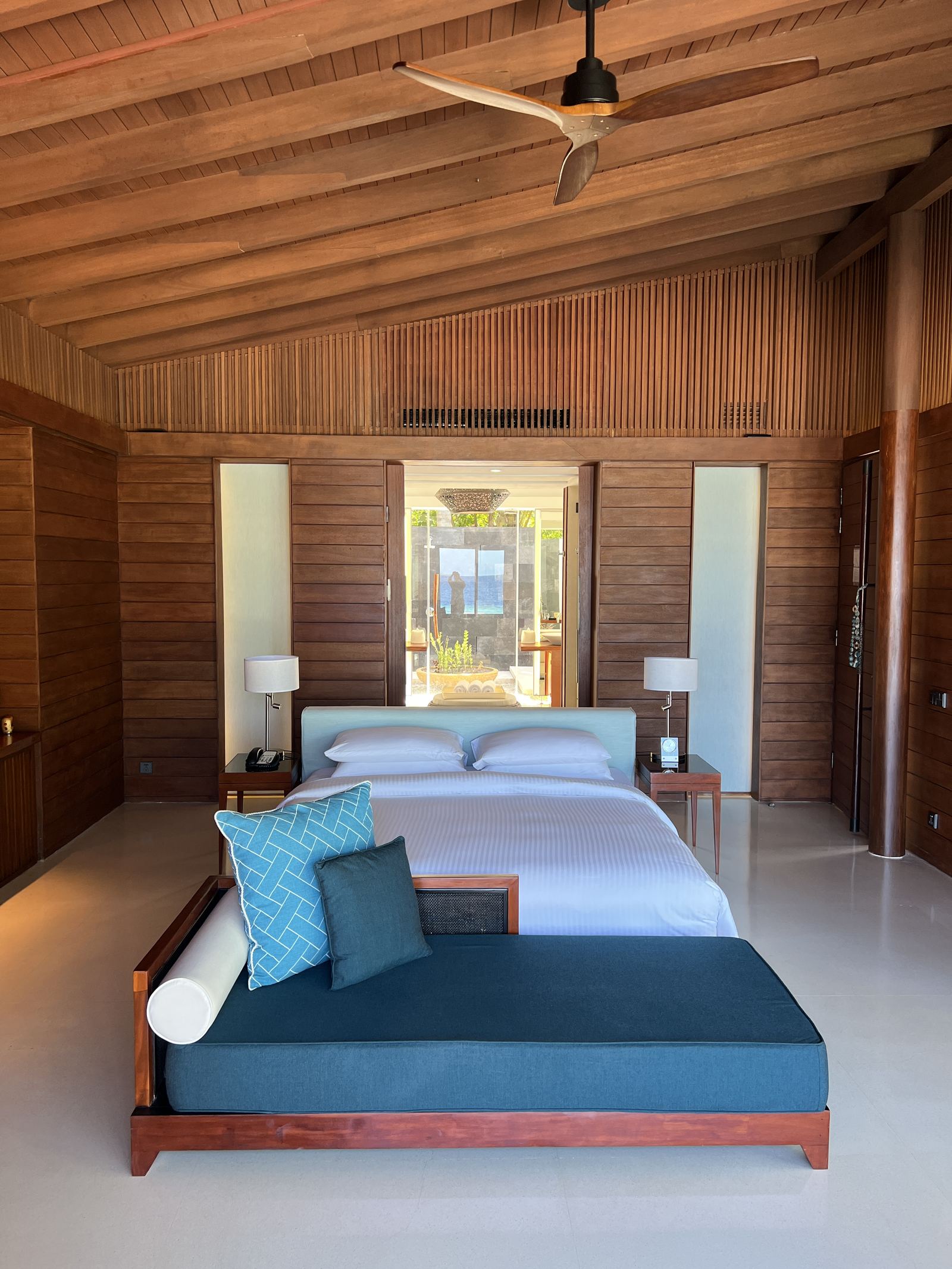 The bedroom of a beach villa with a timber ceiling and the garden beyond