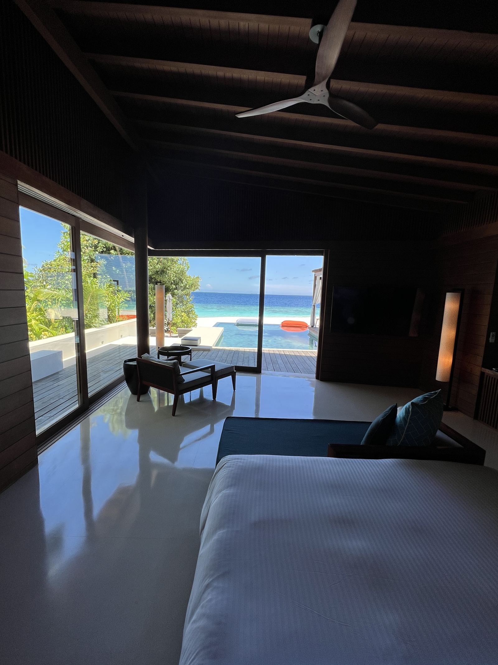The dark timber interior of a beach villa looking out to the pool and the sea