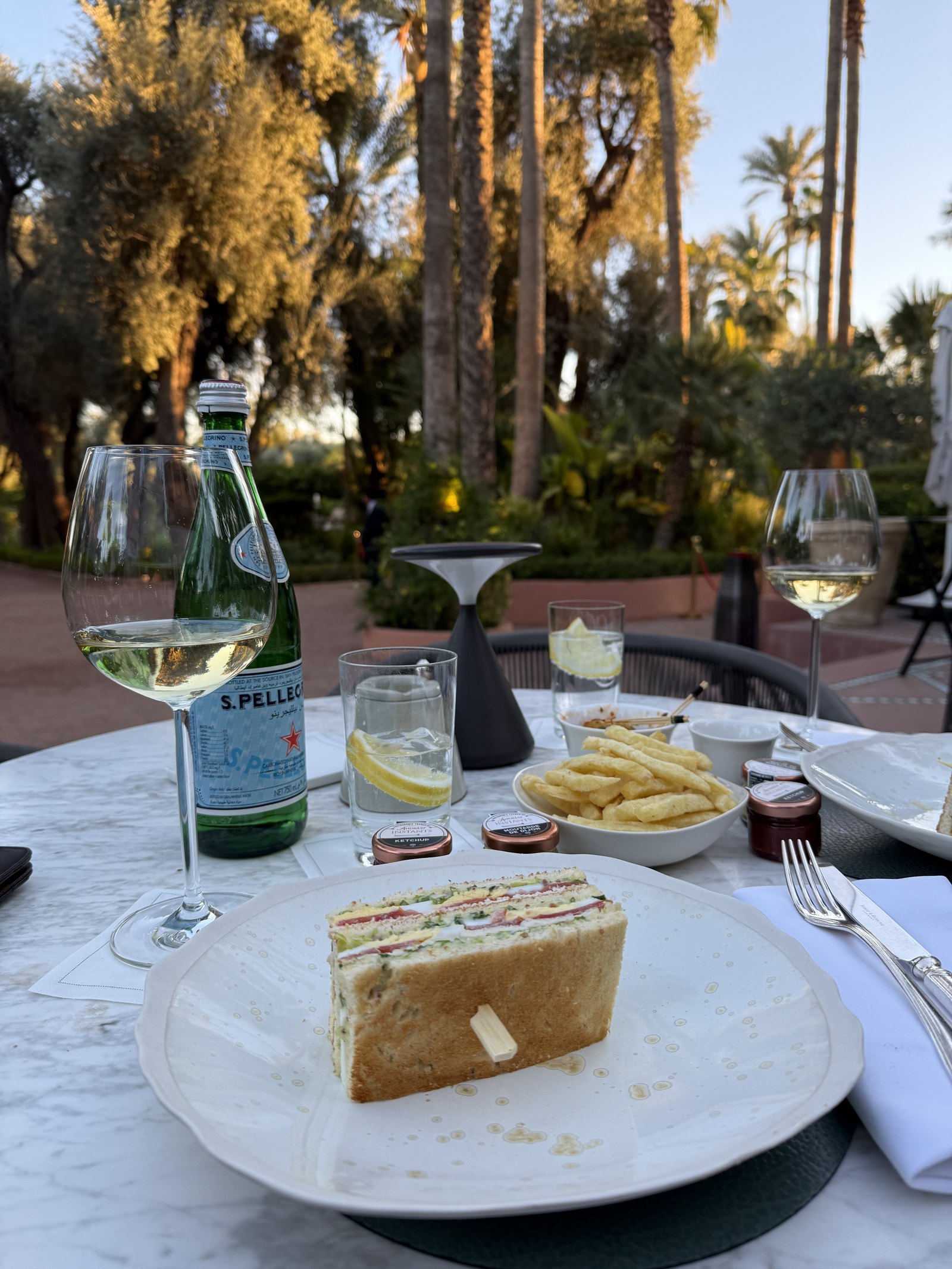 A sandwich on a white plate beside chips, a glass of lemonade and a cup of tea