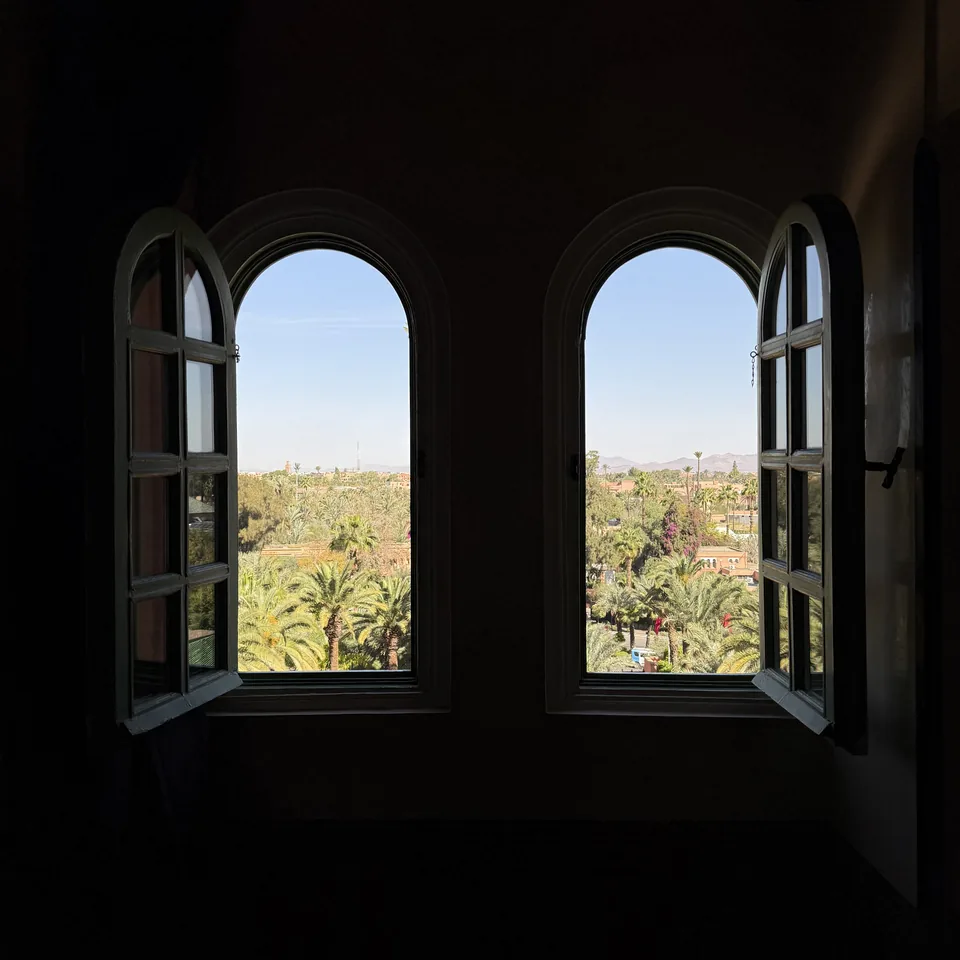 Two open arched windows over the palm grove, seen from a dark room
