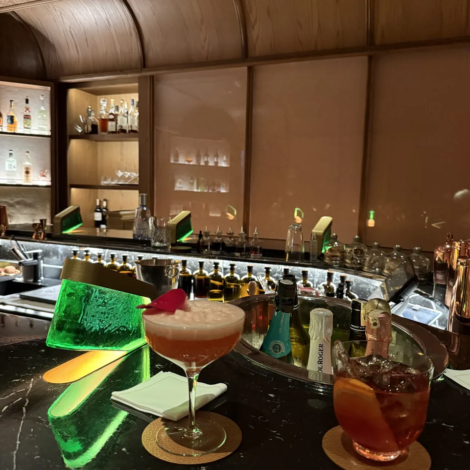 Cocktails on a marble bar counter, with a green glass block and a shelf of bottles behind