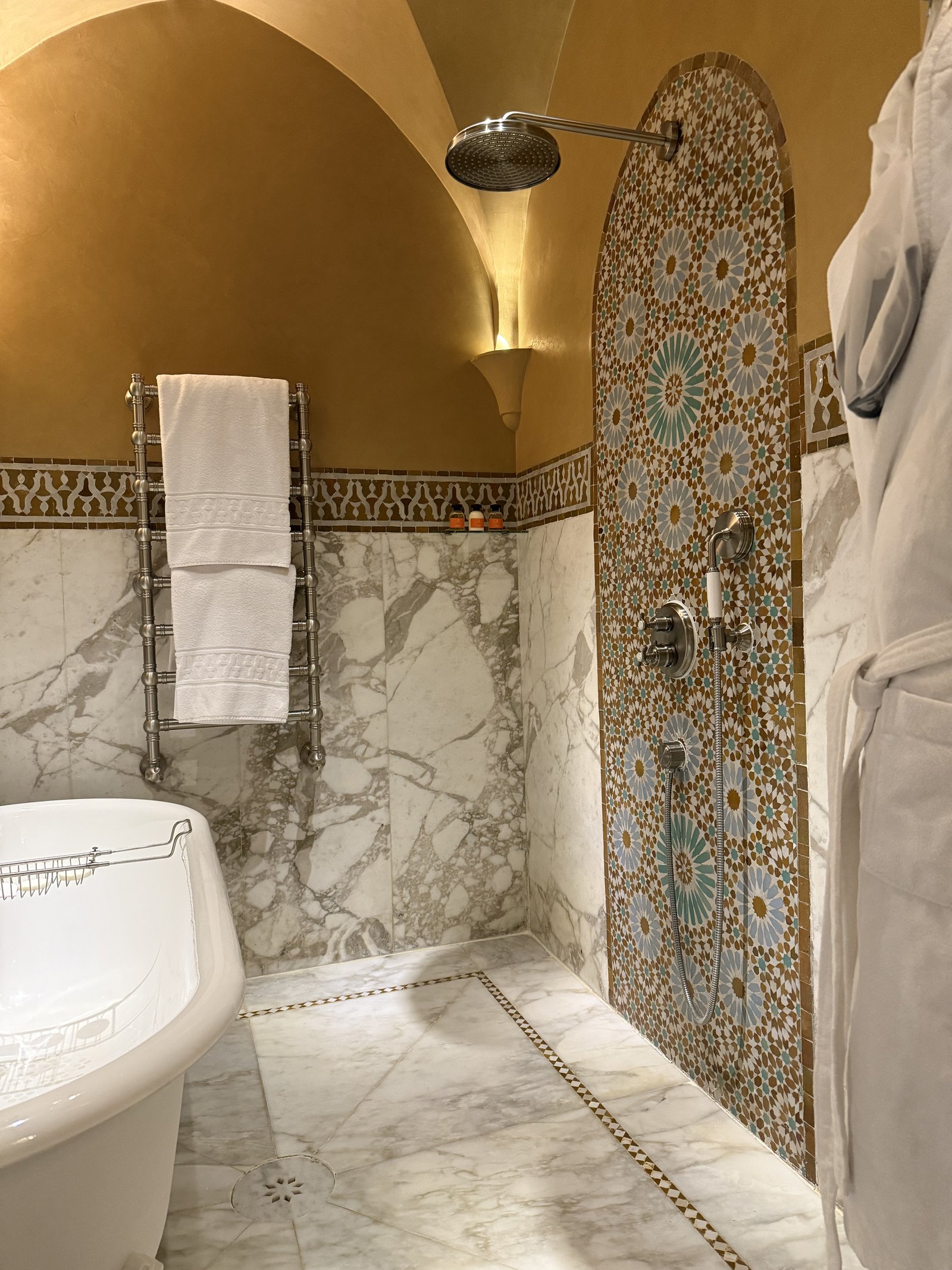A bathroom with white marble walls, a zellige shower panel, a bathtub and a towel rail