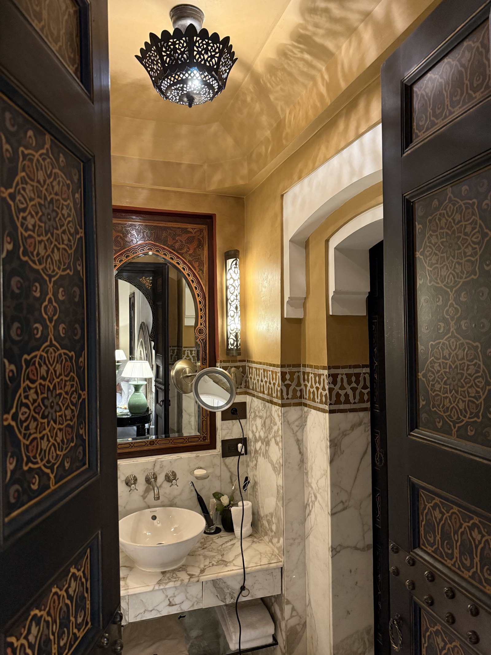 A white basin on a marble counter, with a mirror and a carved wooden door at the edge