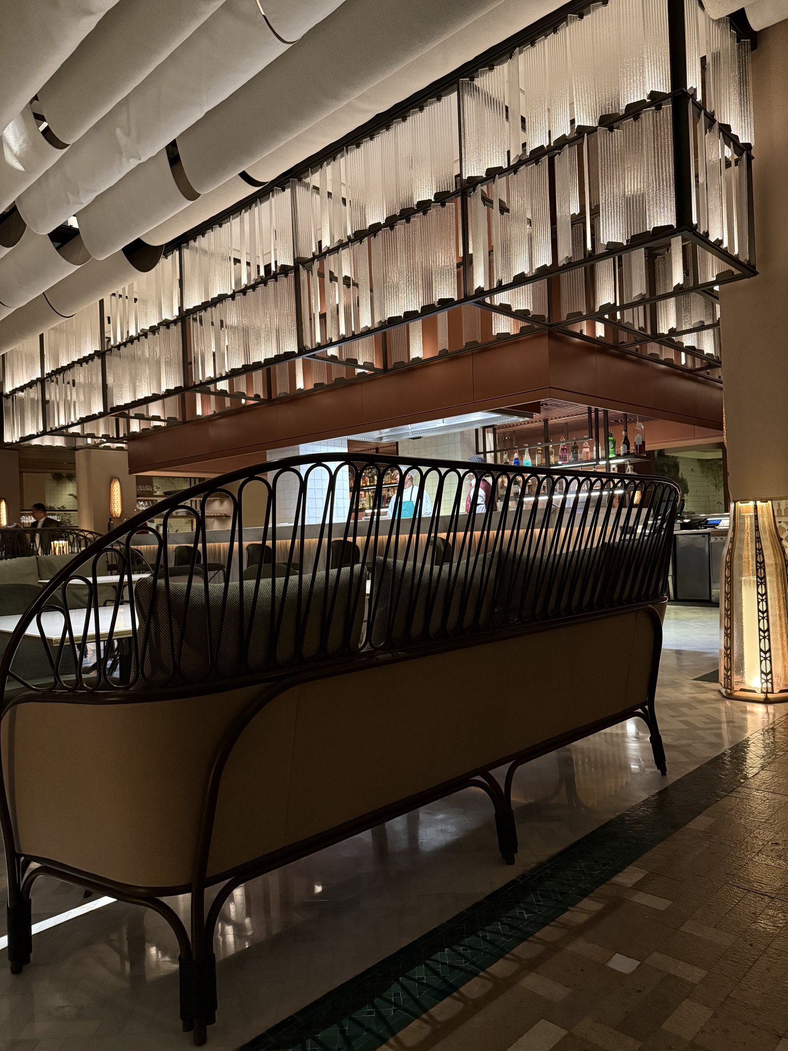 A lounge with a curved black metal bench and leather seats under a lit ceiling of tubes