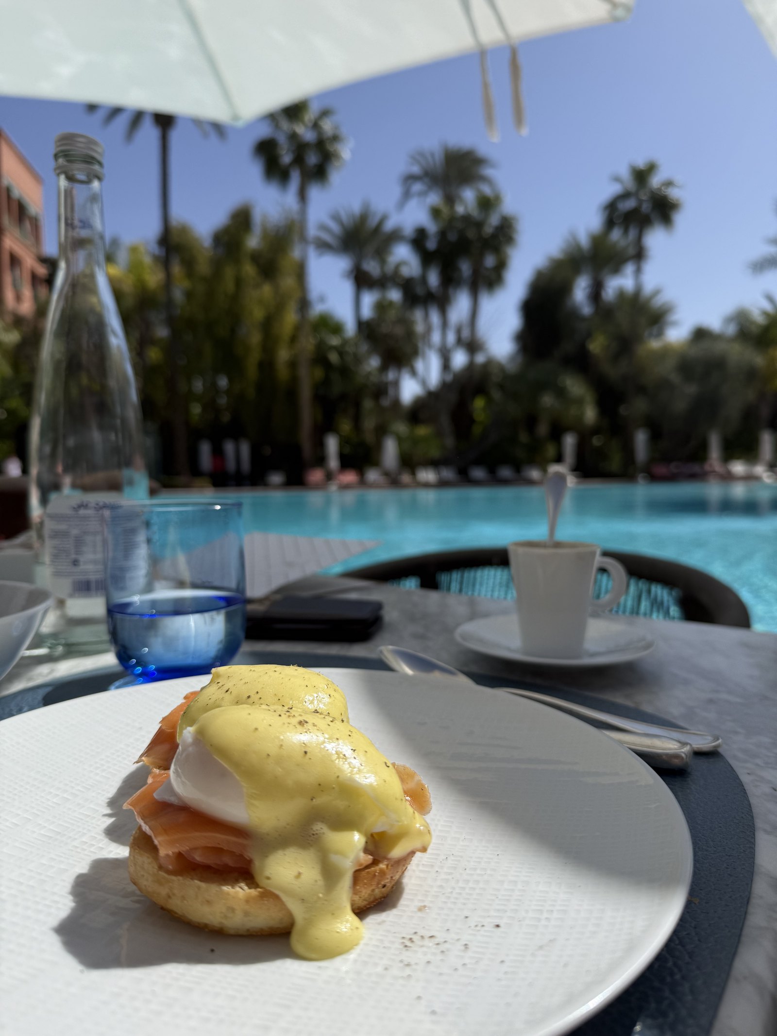 Eggs Benedict with smoked salmon on a white plate, with a glass of water and a cup of coffee beside it