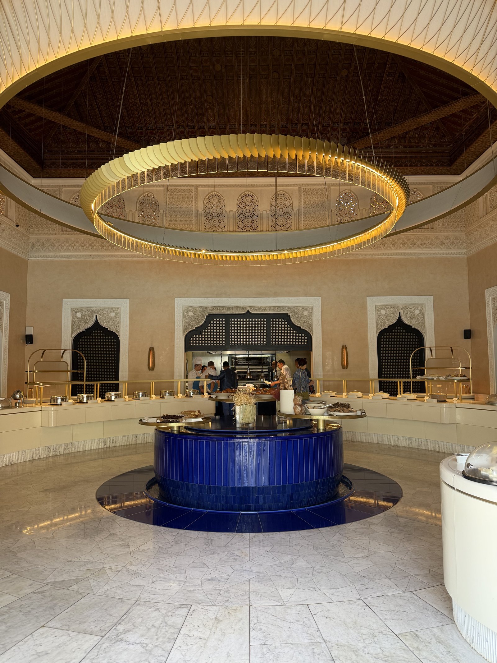 A round buffet counter with a blue central island, copper dishes and a dome of pastries