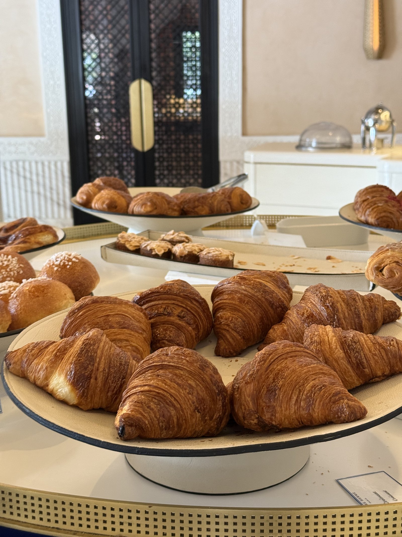Croissants and small pastries arranged on wooden trays, with bread rolls at the edge
