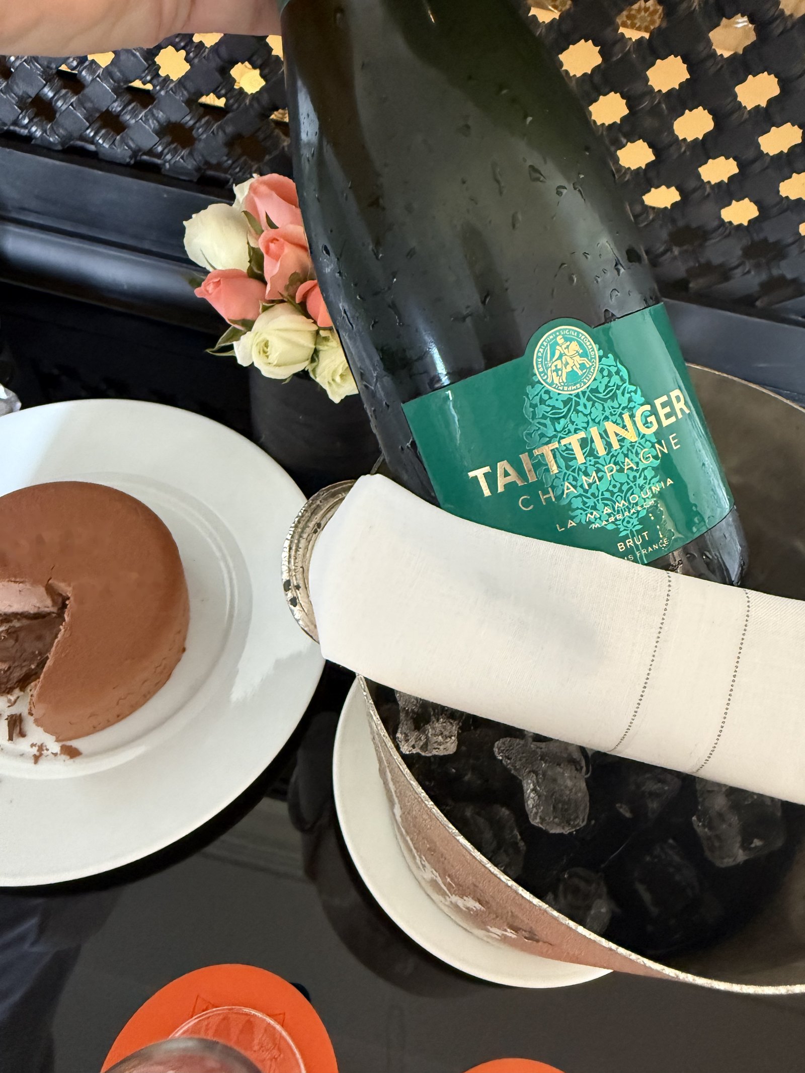 A bottle of champagne in a cloth-wrapped ice bucket, with a chocolate biscuit on a plate