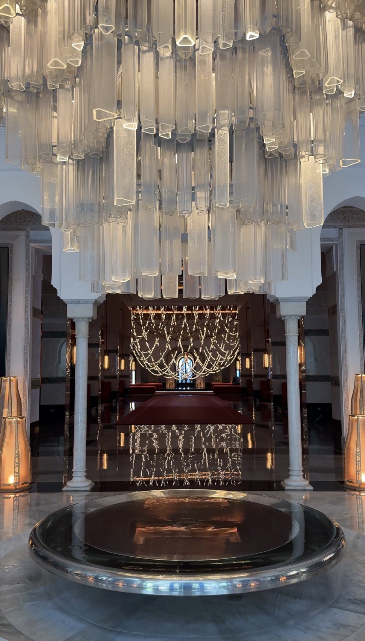 The glass chandelier over the entrance floor, seen between the white marble columns towards the hall beyond