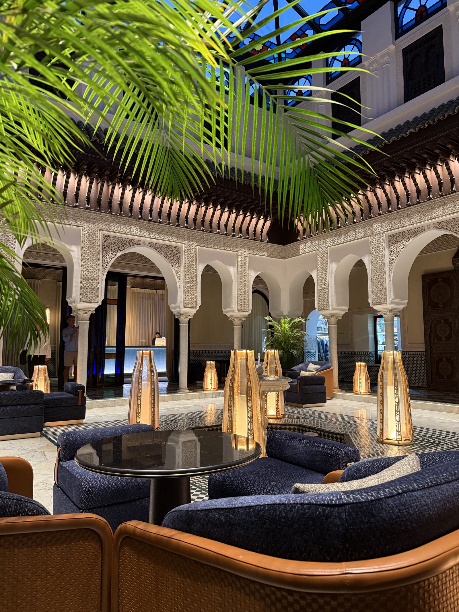 A lounge in a courtyard with blue sofas, a dark table and a lantern on it