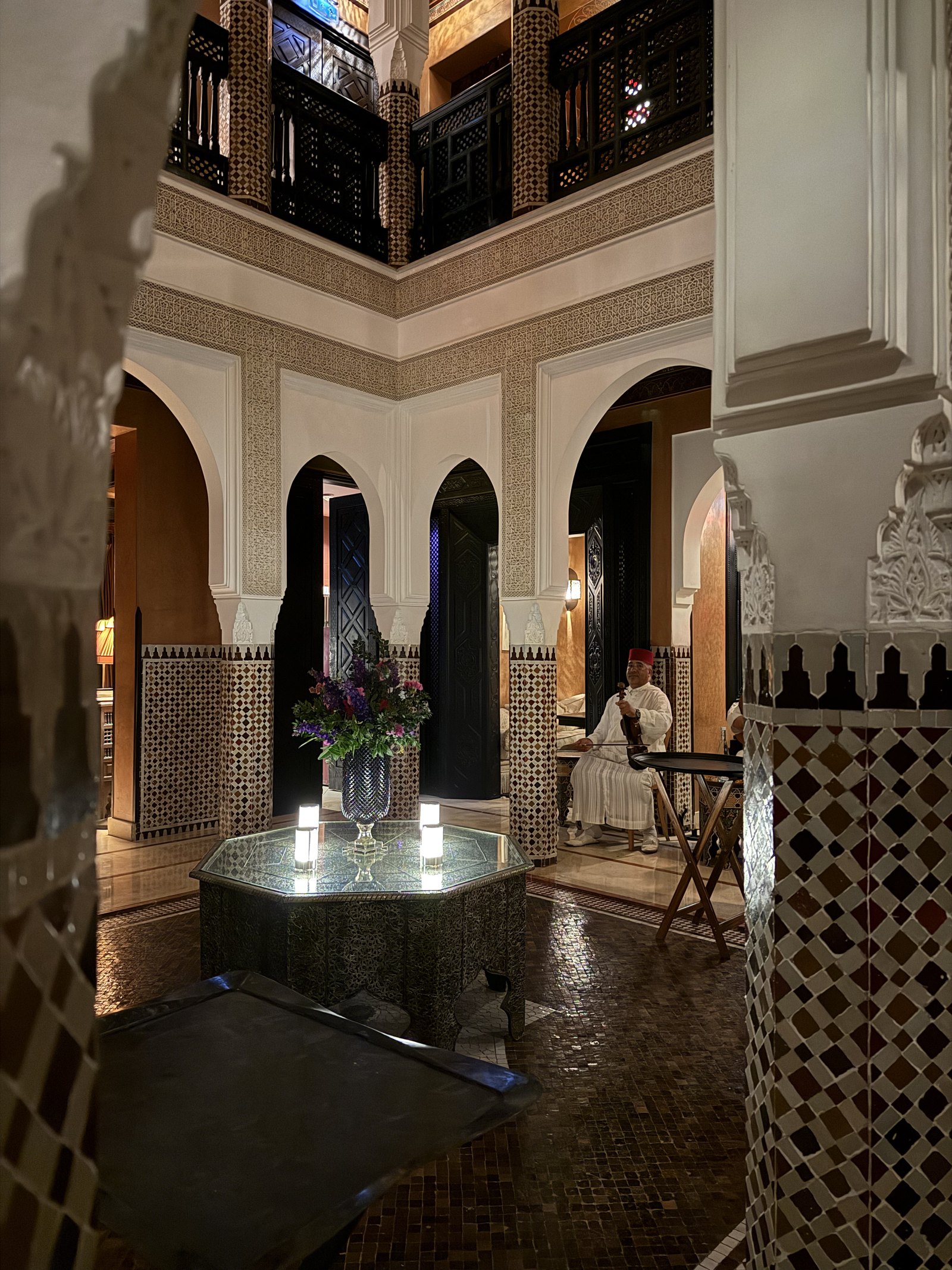 A courtyard at night with a carved wooden ceiling, arches and a lantern hanging over the floor