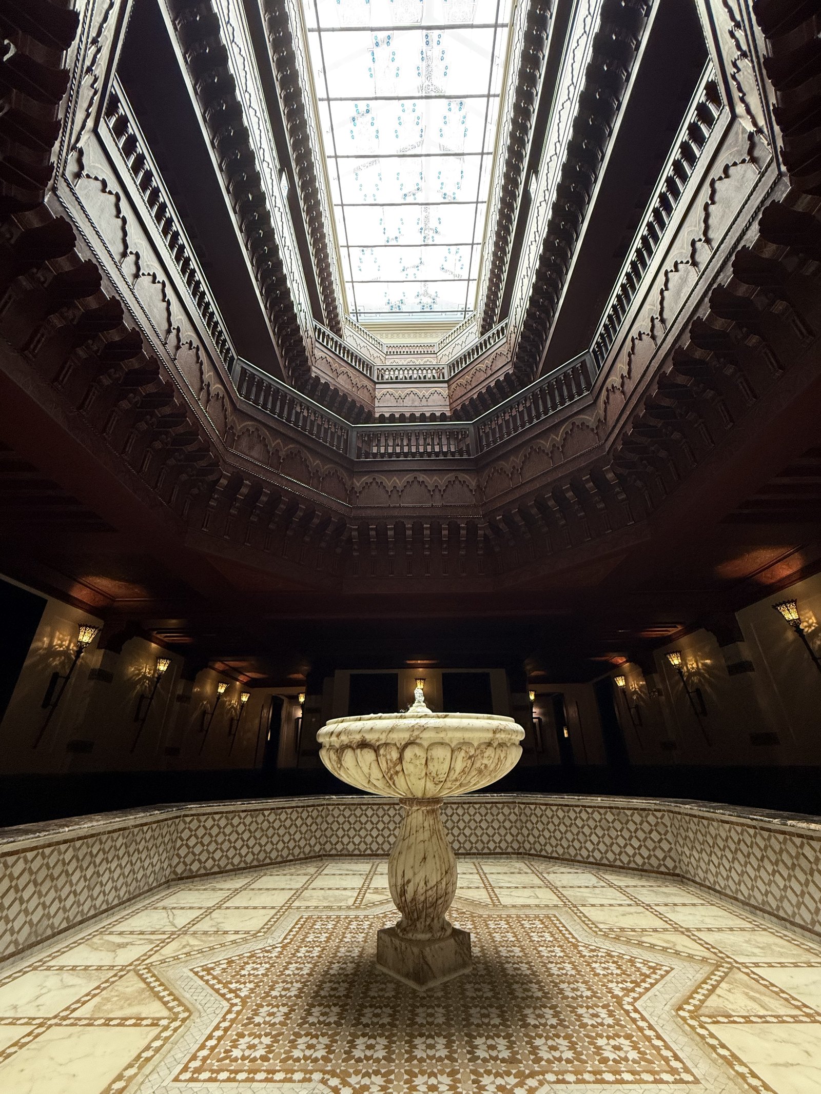 A carved wooden dome above a marble fountain, with a patterned floor beneath
