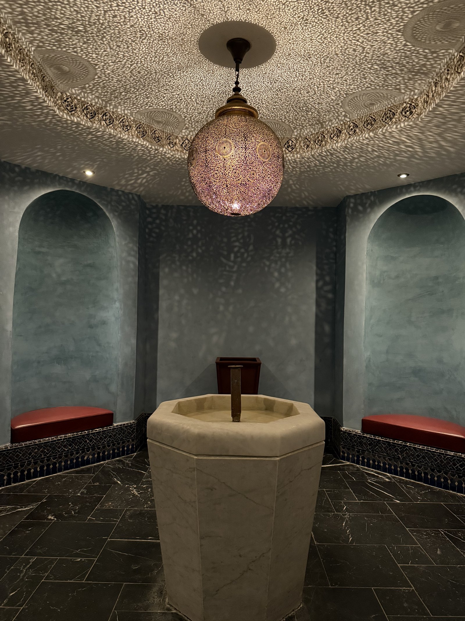 A pale octagonal marble basin in a room with green walls, red benches and a lantern above