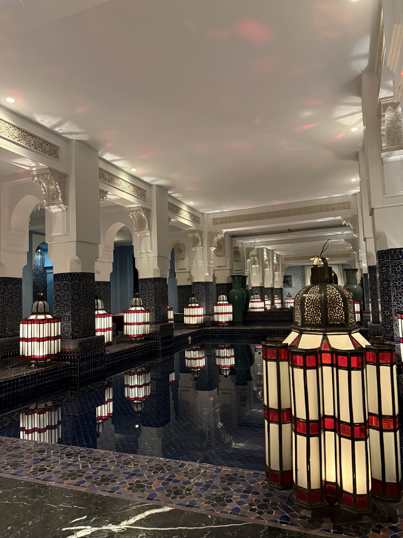 Red and white lanterns standing over a dark pool with arches reflected in its surface
