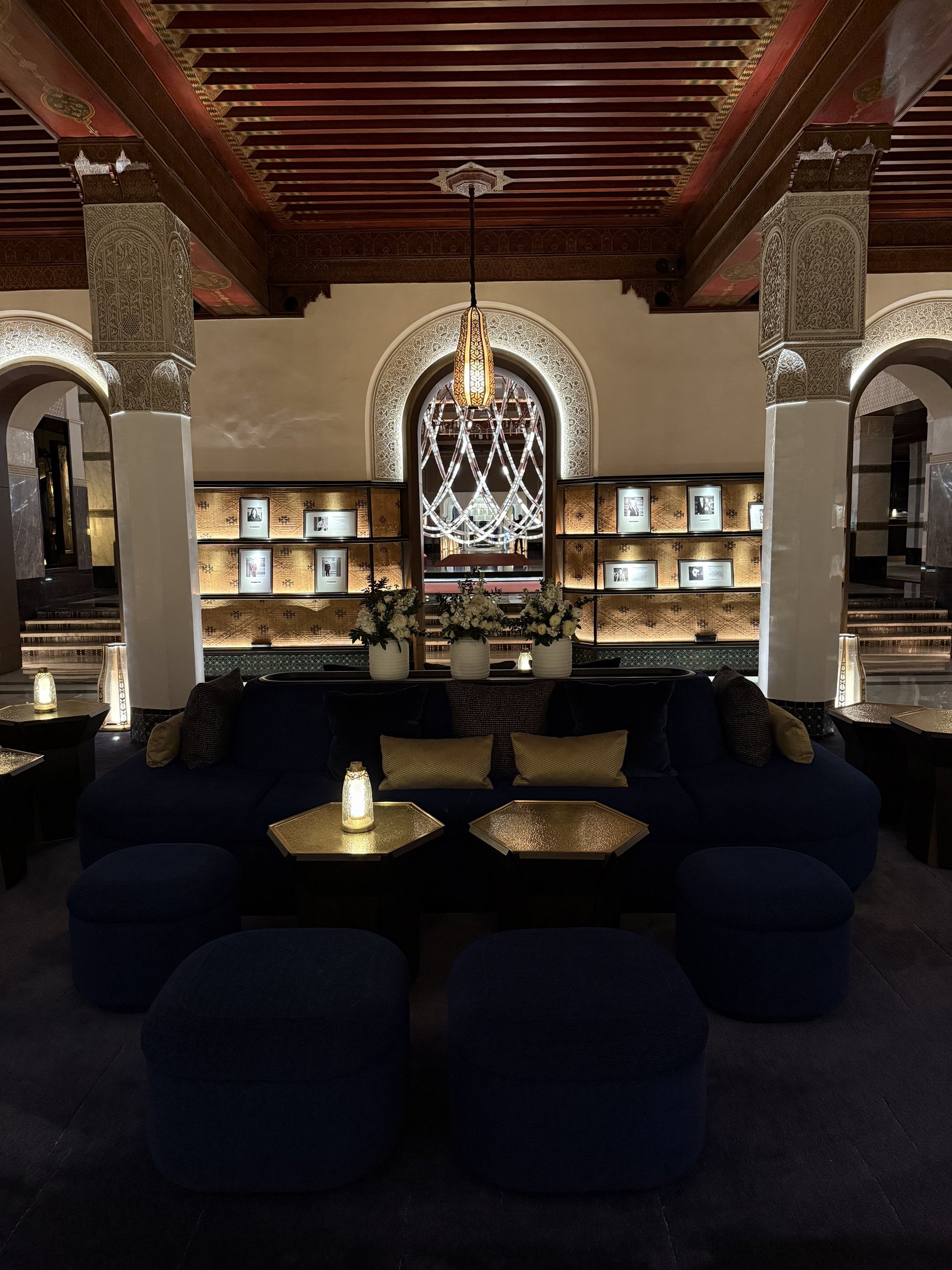A lounge with navy velvet pouffes, gold side tables and a lit chandelier behind