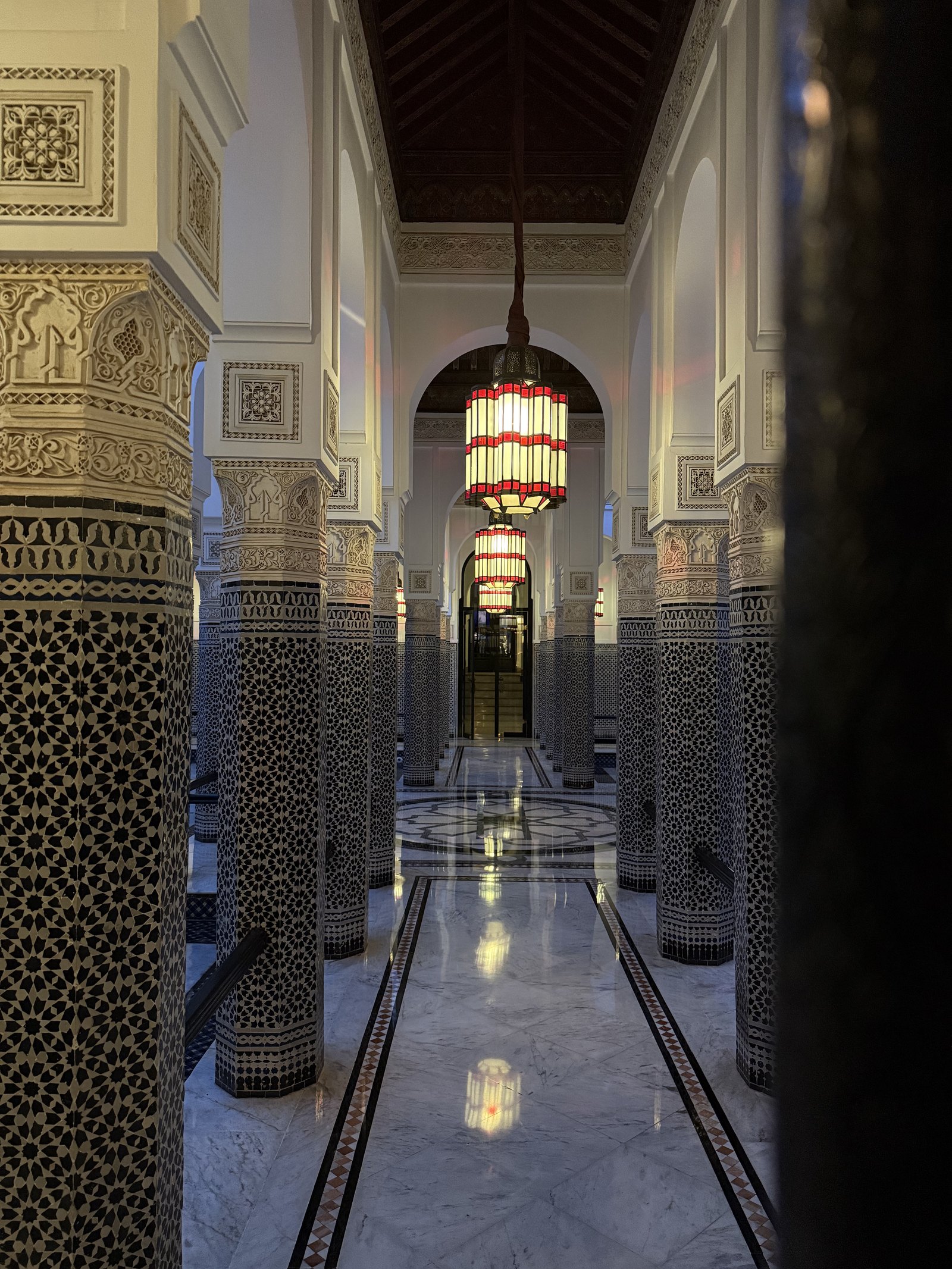 A long corridor with mosaic columns, arches and a red lantern at the far end