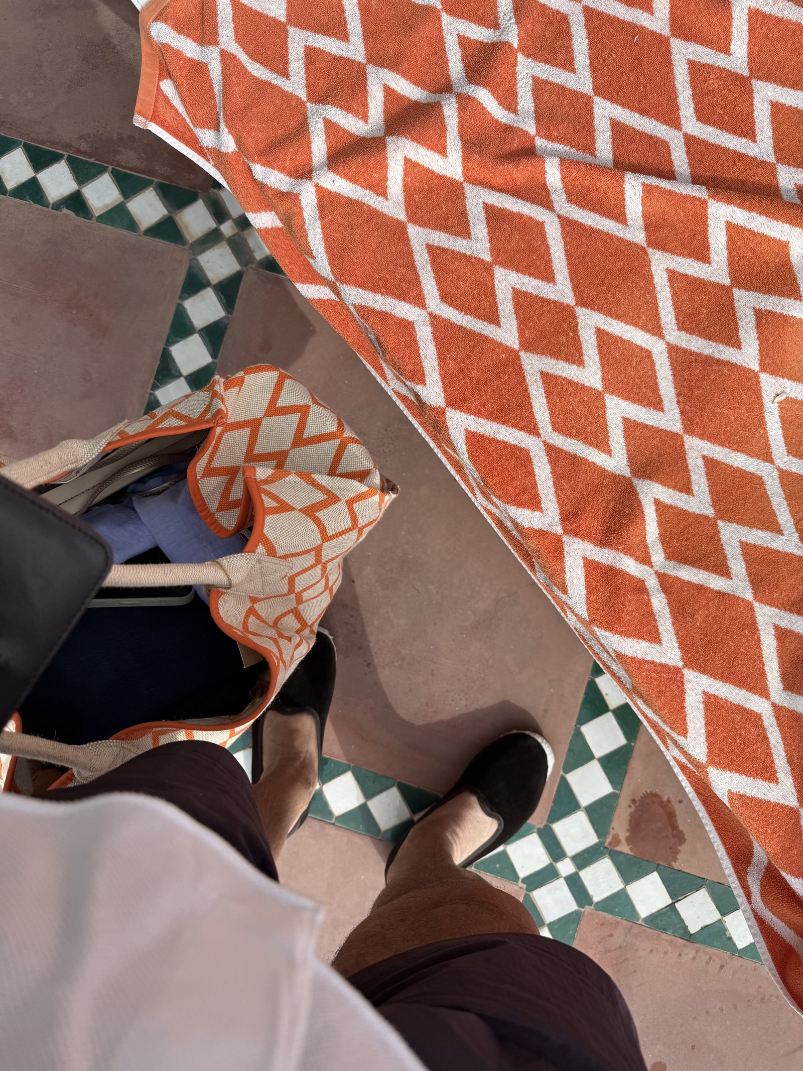 Orange-and-white woven cloth, a handbag and a pair of heels on a green and white tiled floor, seen from above