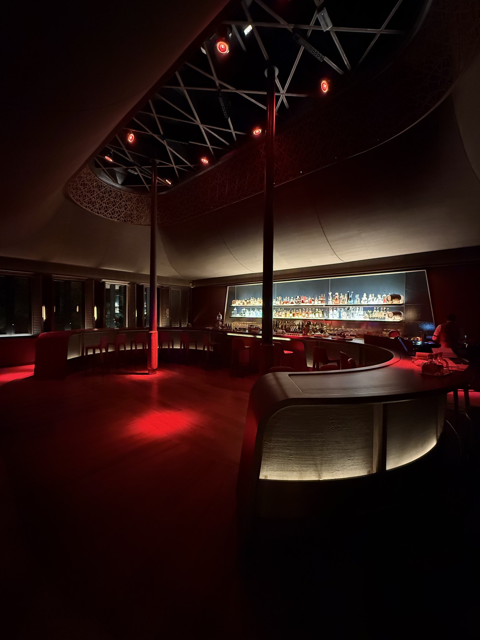 A curved bar in a dark red room, with its counter lit from beneath