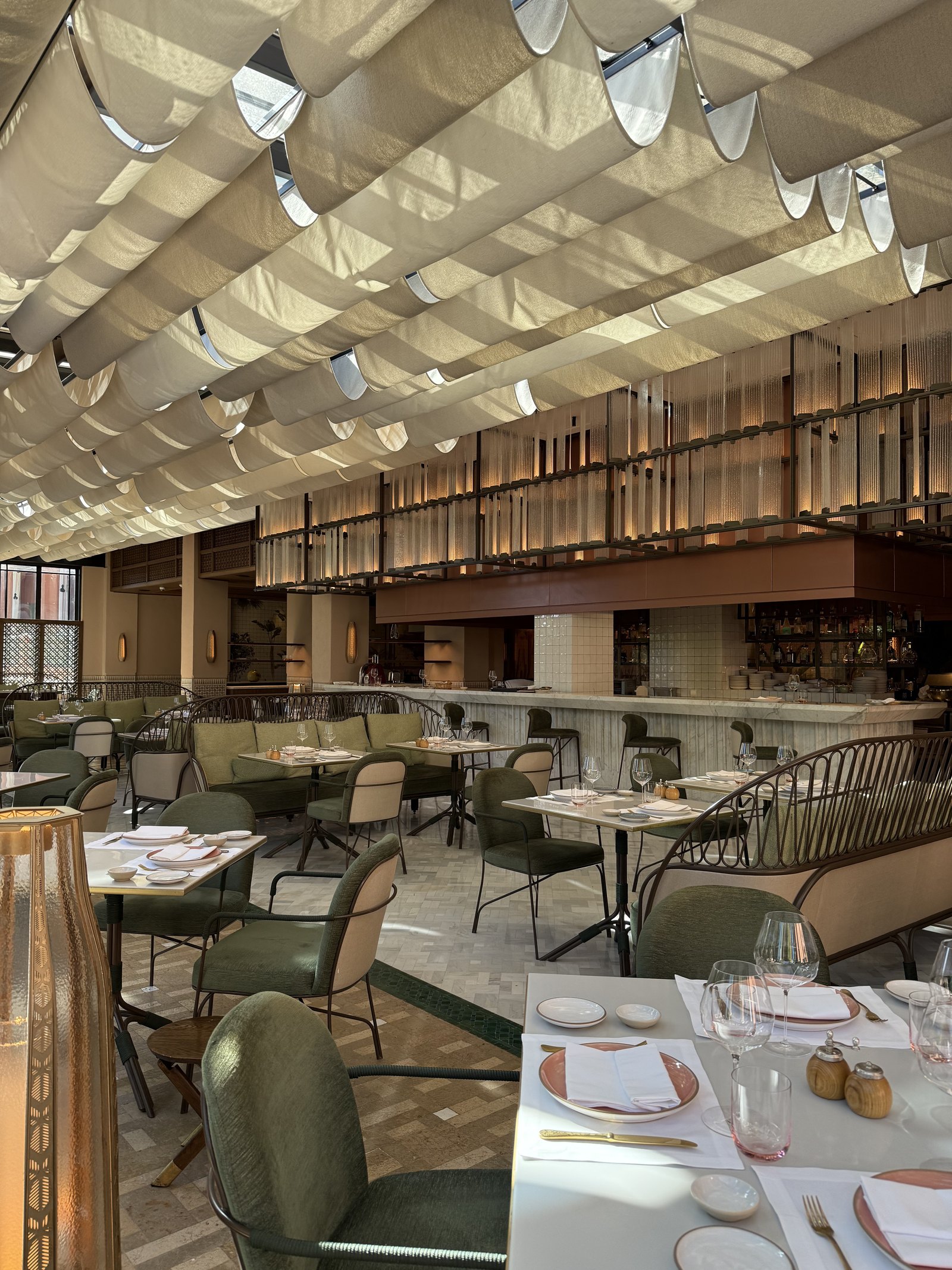 A dining room under a sculpted canvas canopy, with tables set for lunch and green chairs