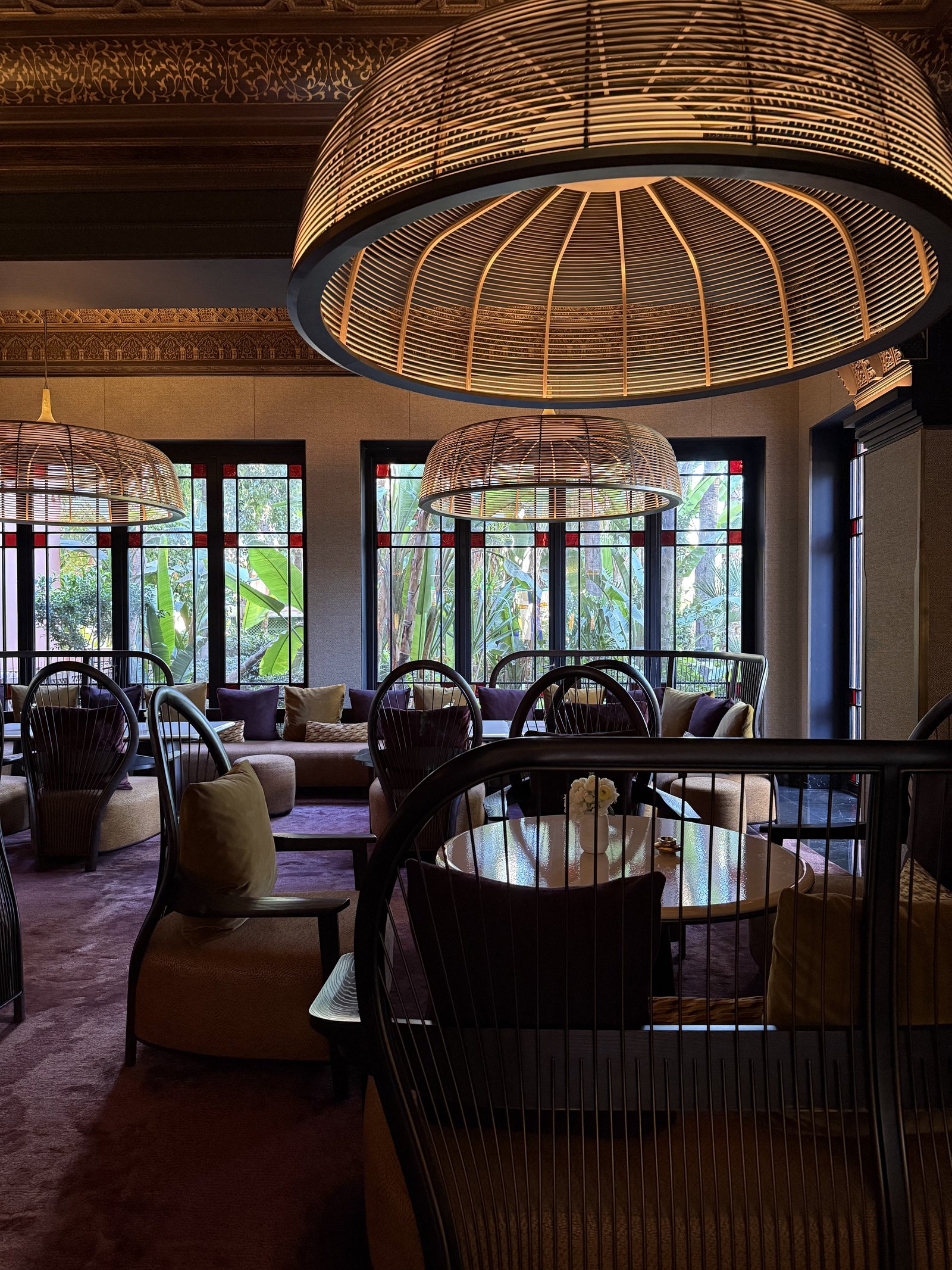 A dining room with wicker pendant lamps over a bench of brown leather and high windows onto the garden