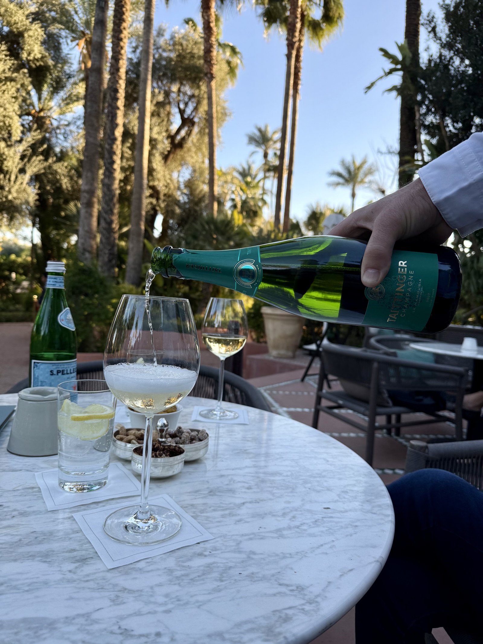 Champagne being poured into a glass on a marble table in the garden, with water and nuts beside it