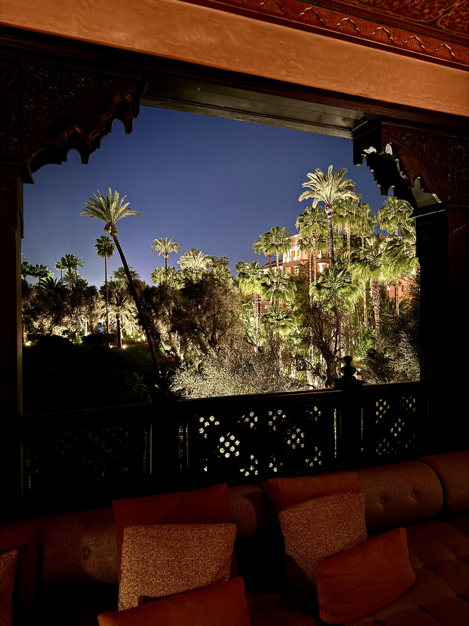 A terrace at night with orange cushions on a low sofa and the garden lit below