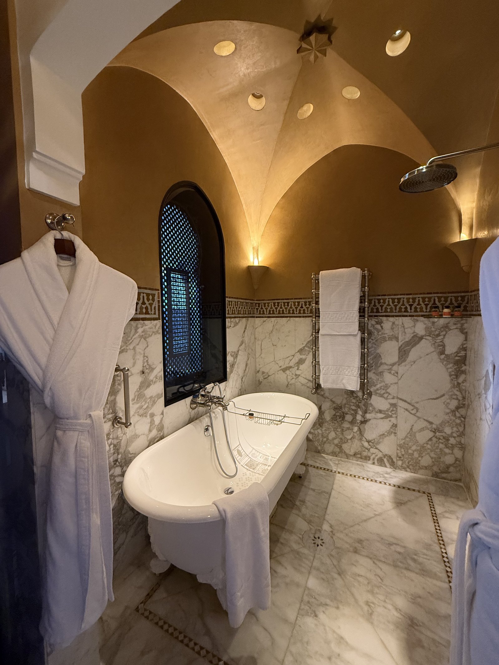 A freestanding bathtub with white robes hung on a hook beside it