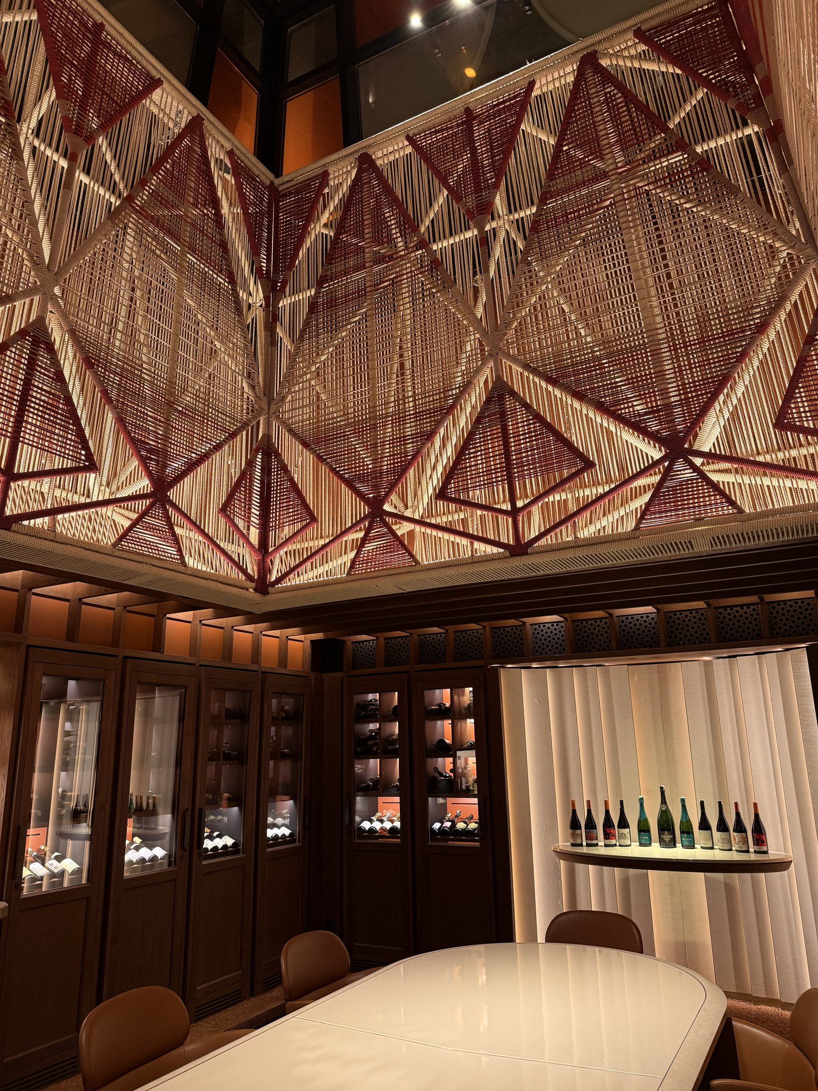 A wine room with glass cabinets, a long white table and bottles lit on a shelf
