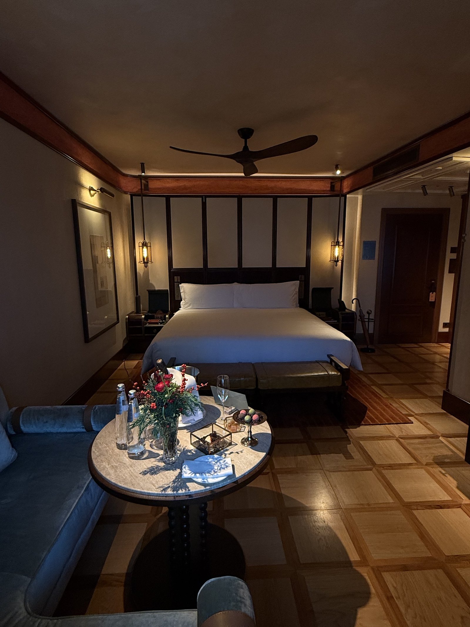 A bed under a timber canopy frame with a ceiling fan and a table set in the foreground