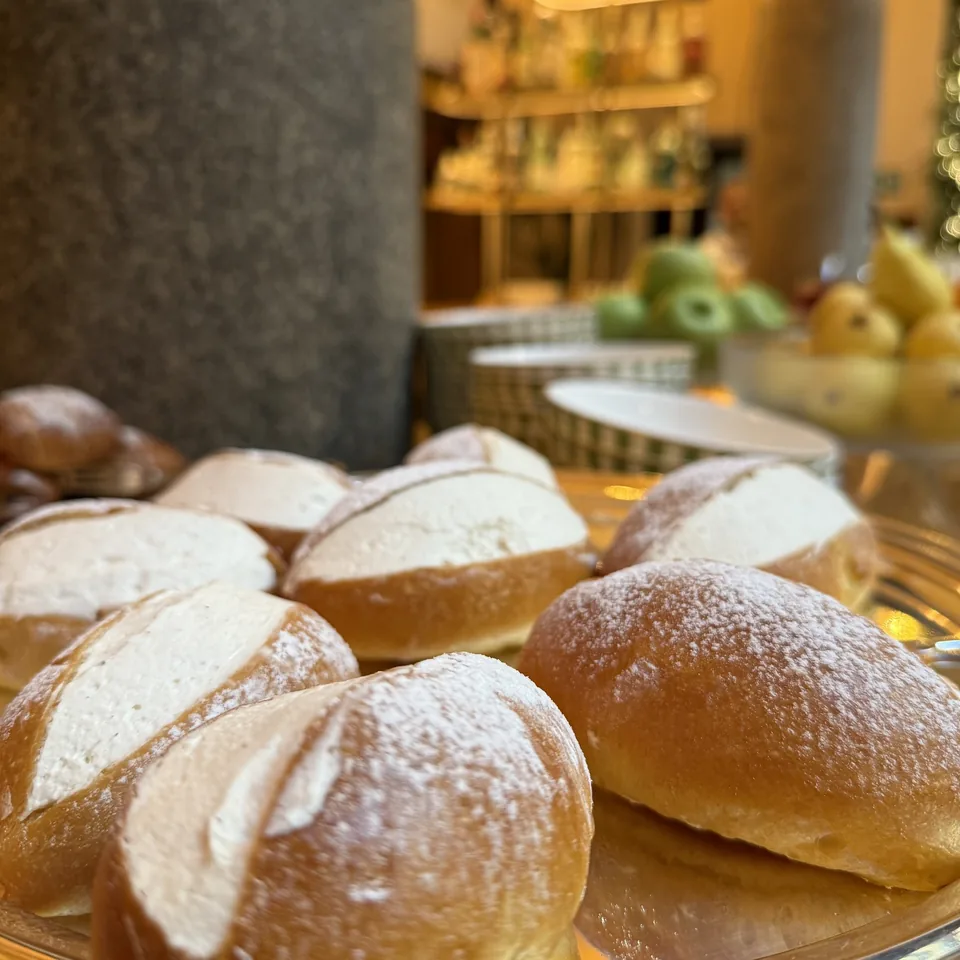 Maritozzi and bomboloni dusted with sugar on a glass stand at breakfast
