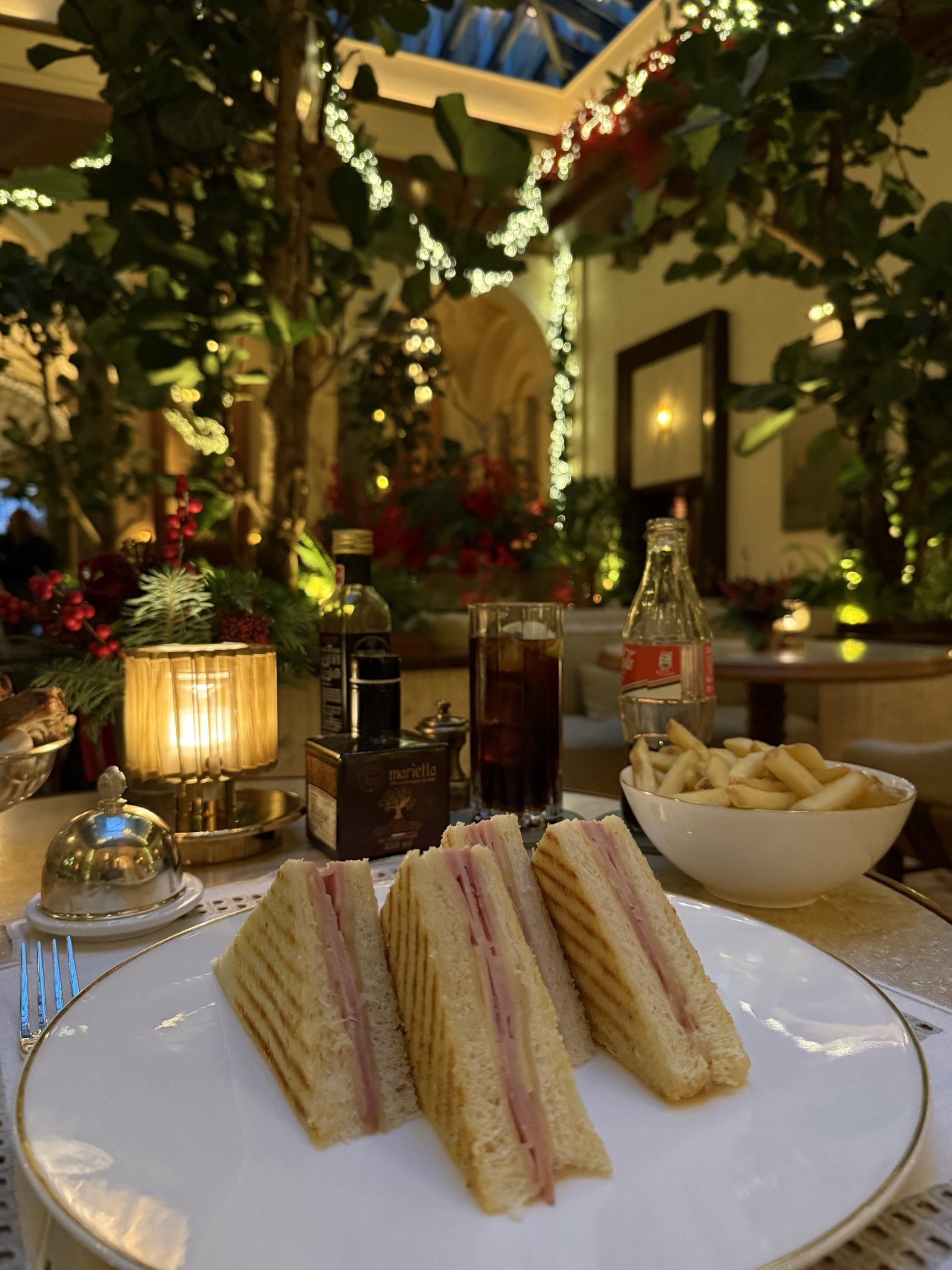 A club sandwich with crisps and a dark drink on a table among the lit greenery
