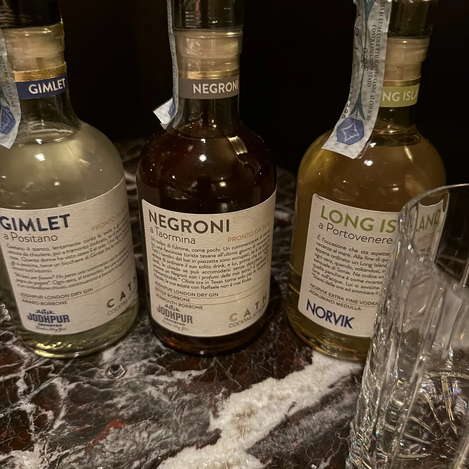Three bottled cocktails labelled La Minerva standing on dark marble