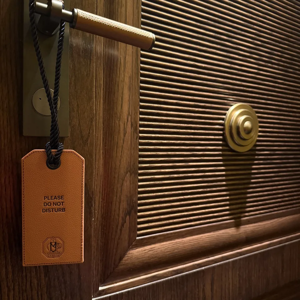 A leather do not disturb tag hanging from the handle of a fluted timber door