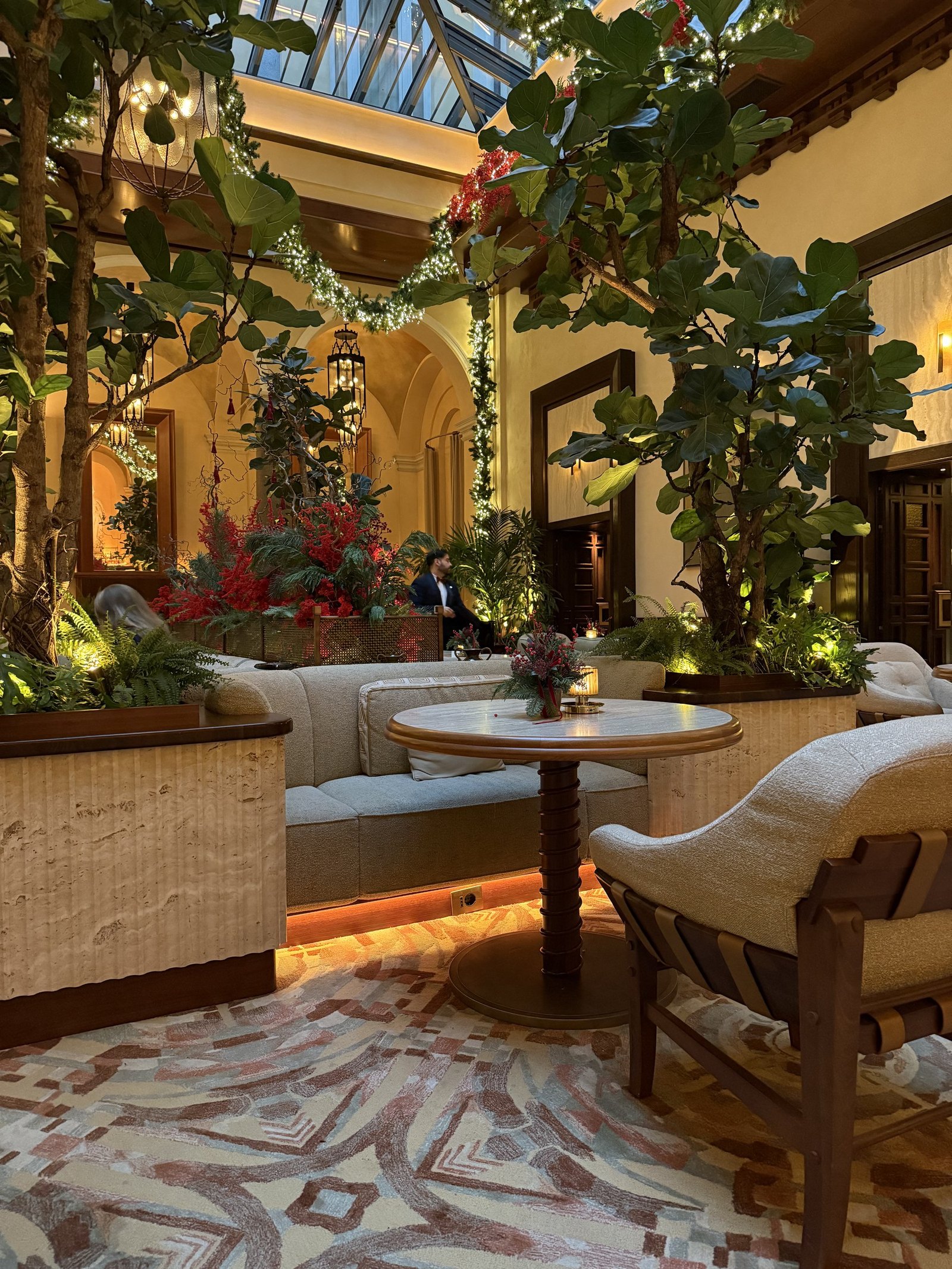 A seating area under trees and greenery hung with lights and red berries