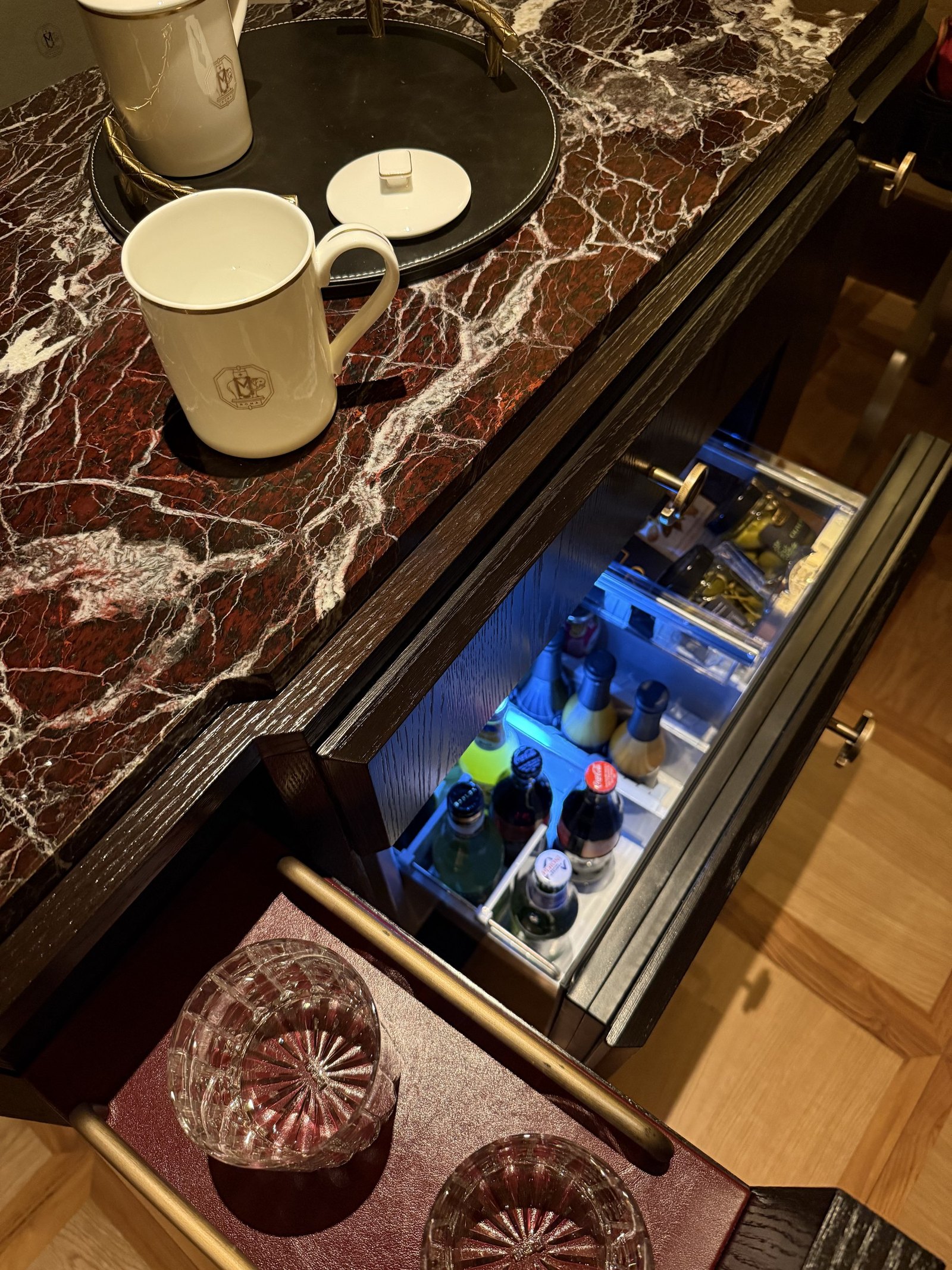 A red marble pantry with cups, a tray and the minibar drawer open below
