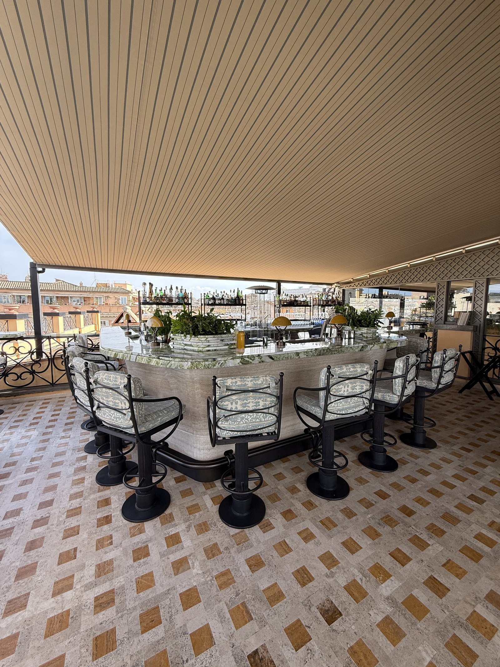 The rooftop bar counter with stools, flowers and a patterned tile floor in daylight