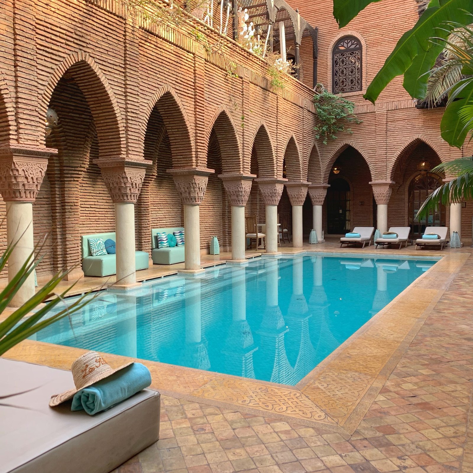 The pool at La Sultana lying between brick arcades of carved columns and horseshoe arches, with daybeds along the far side in late afternoon light