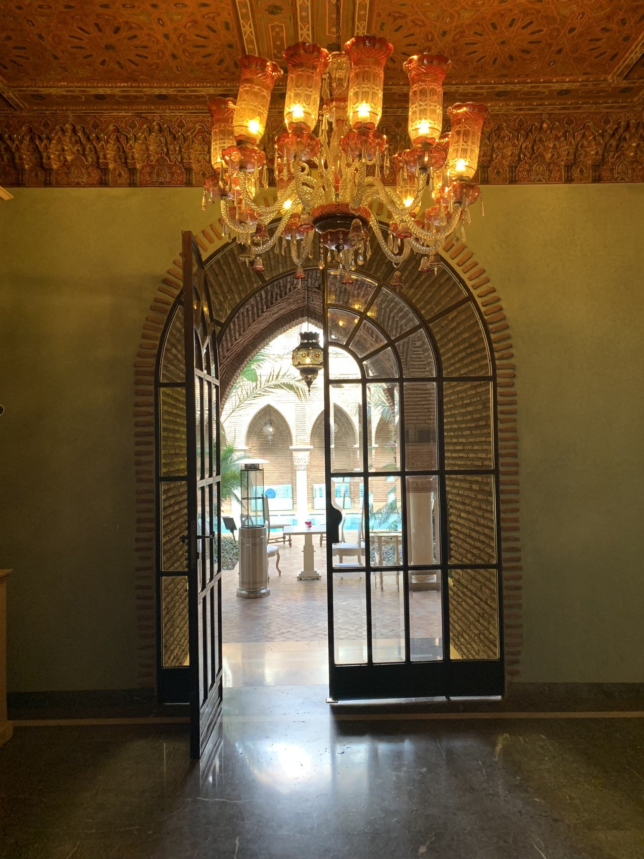 A tall arched glass door at La Sultana opening onto a courtyard with the pool beyond