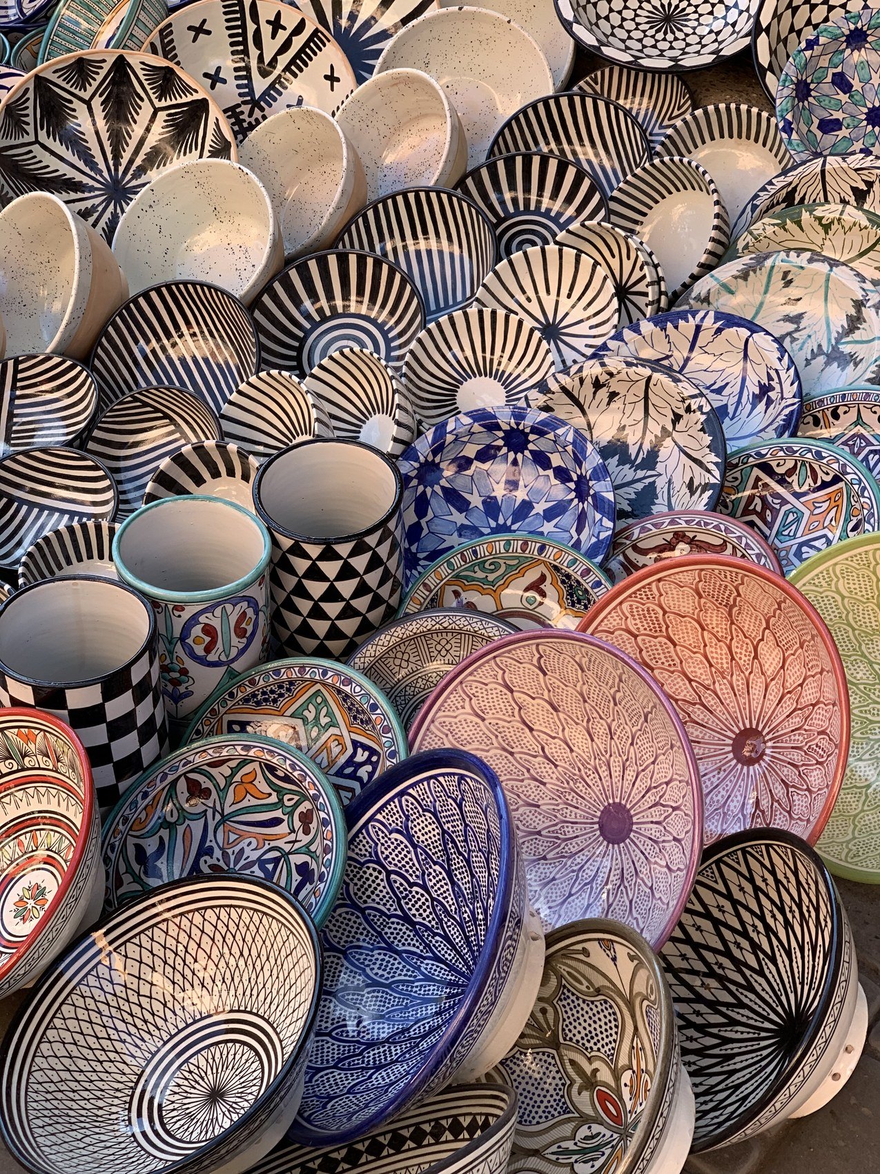 Stacks of hand painted Moroccan bowls and plates in blue, black and pink patterns in a souk