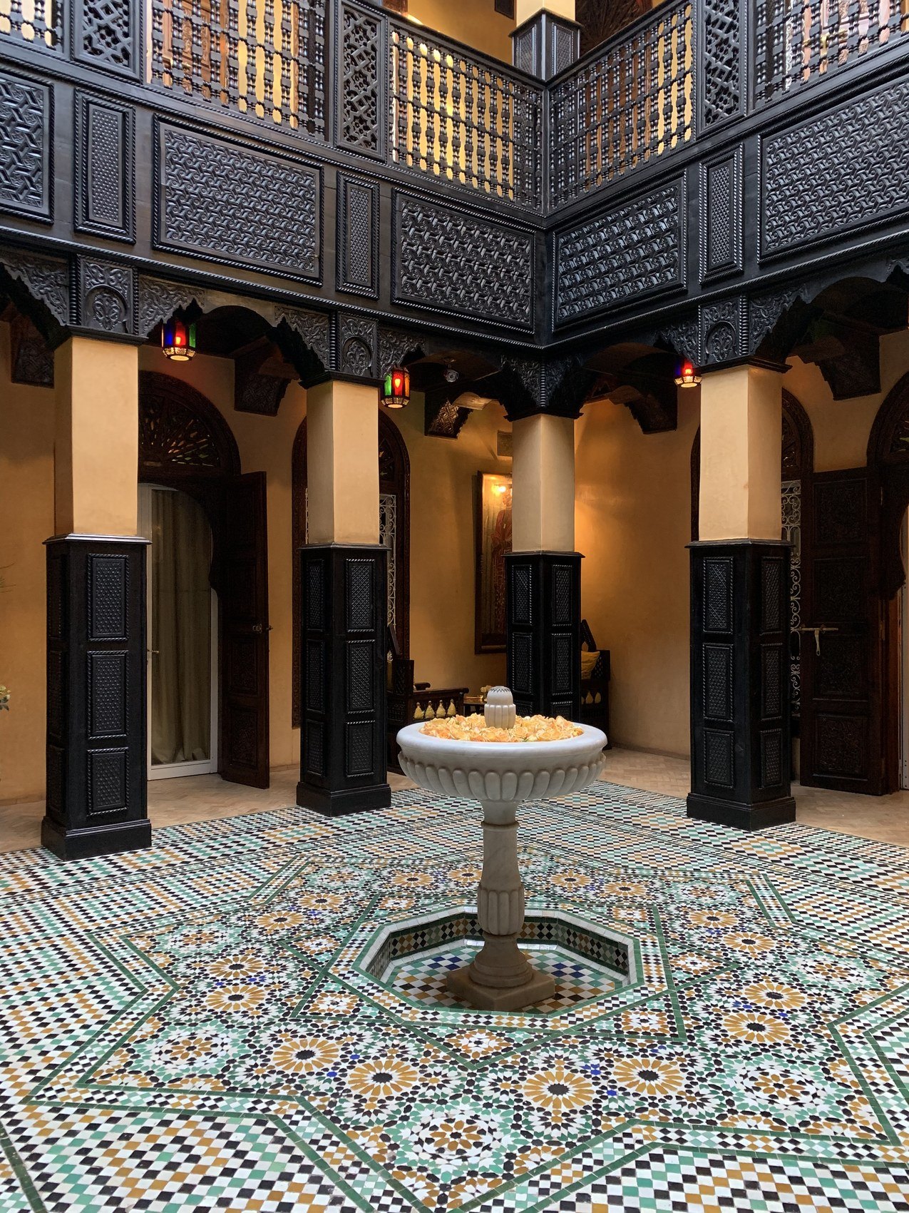 A tiled courtyard at La Sultana at night with a carved stone fountain at the centre and lanterns in the arcades
