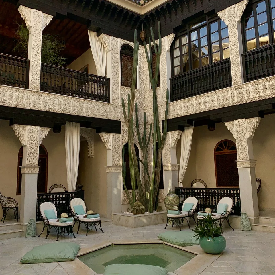 A galleried courtyard at La Sultana with carved timber balconies, a cactus and a shallow green pool