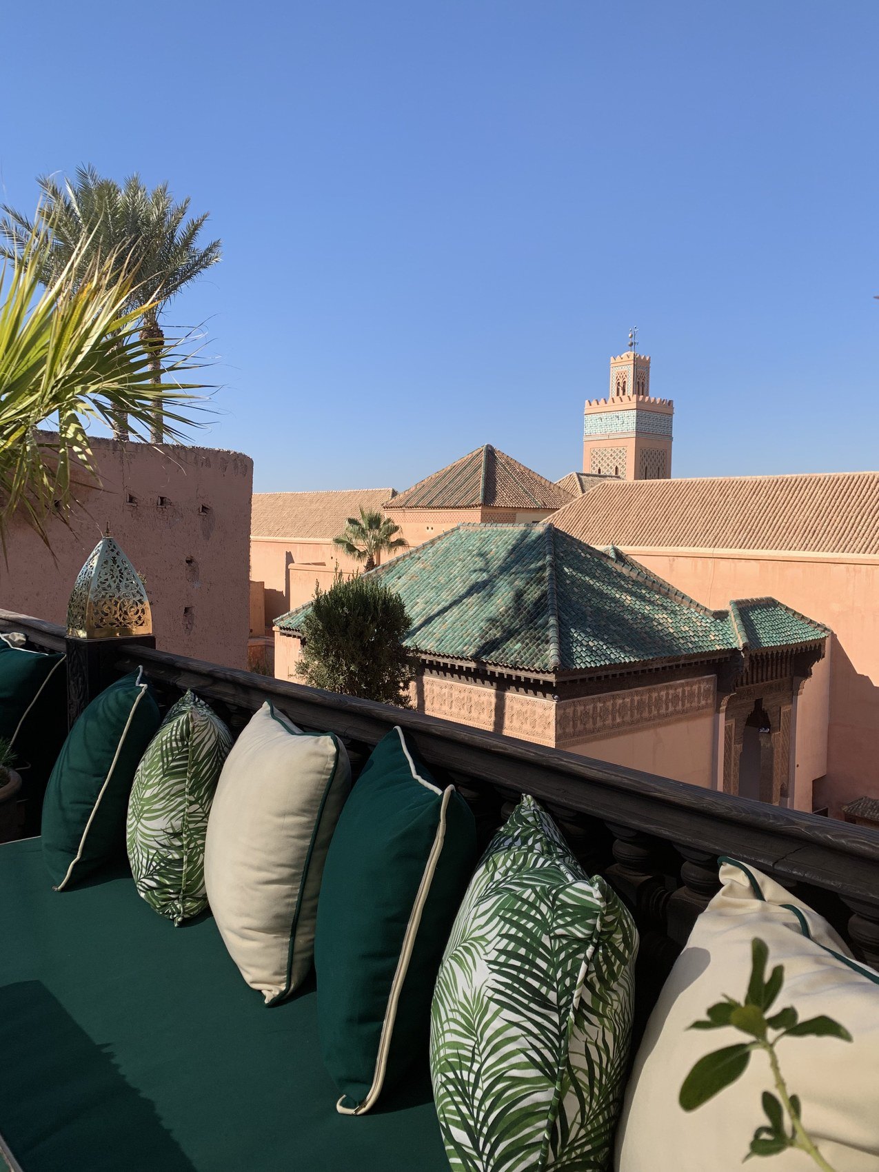 Green and palm printed cushions on a rooftop banquette at La Sultana looking over green tiled roofs to the minaret