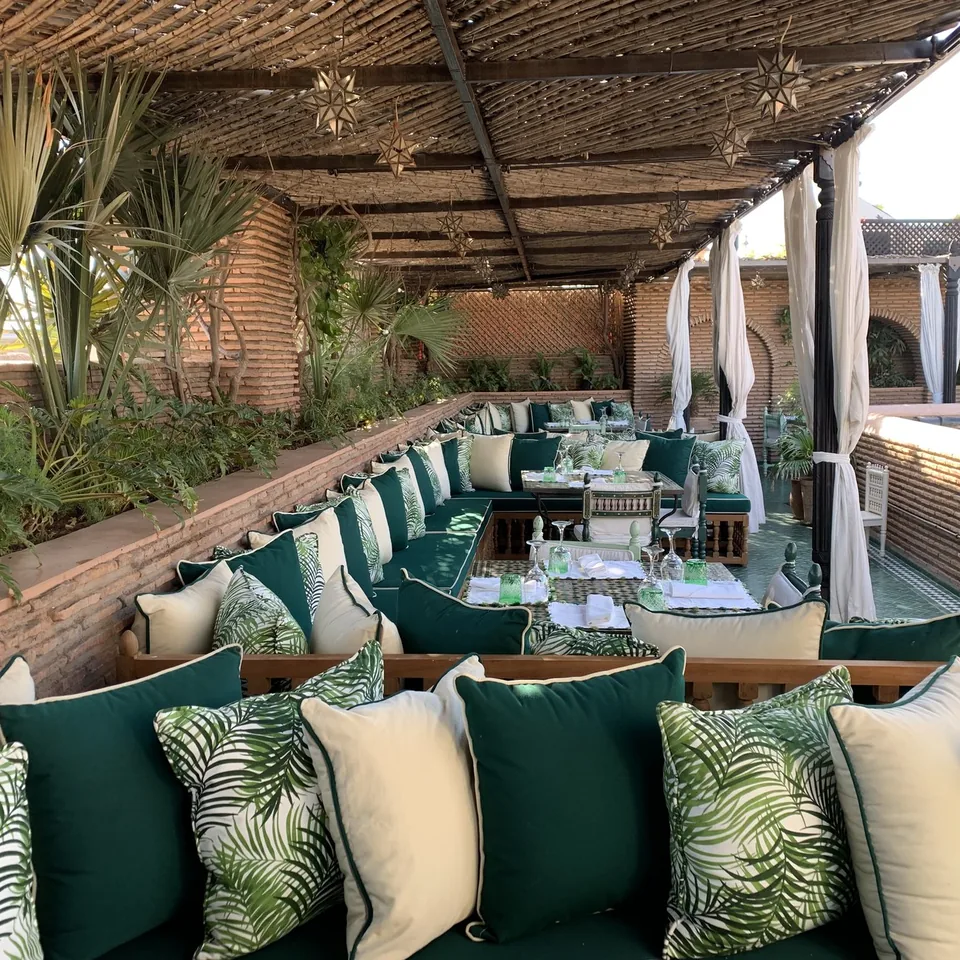 A long banquette of green and palm printed cushions under a cane roof at La Sultana