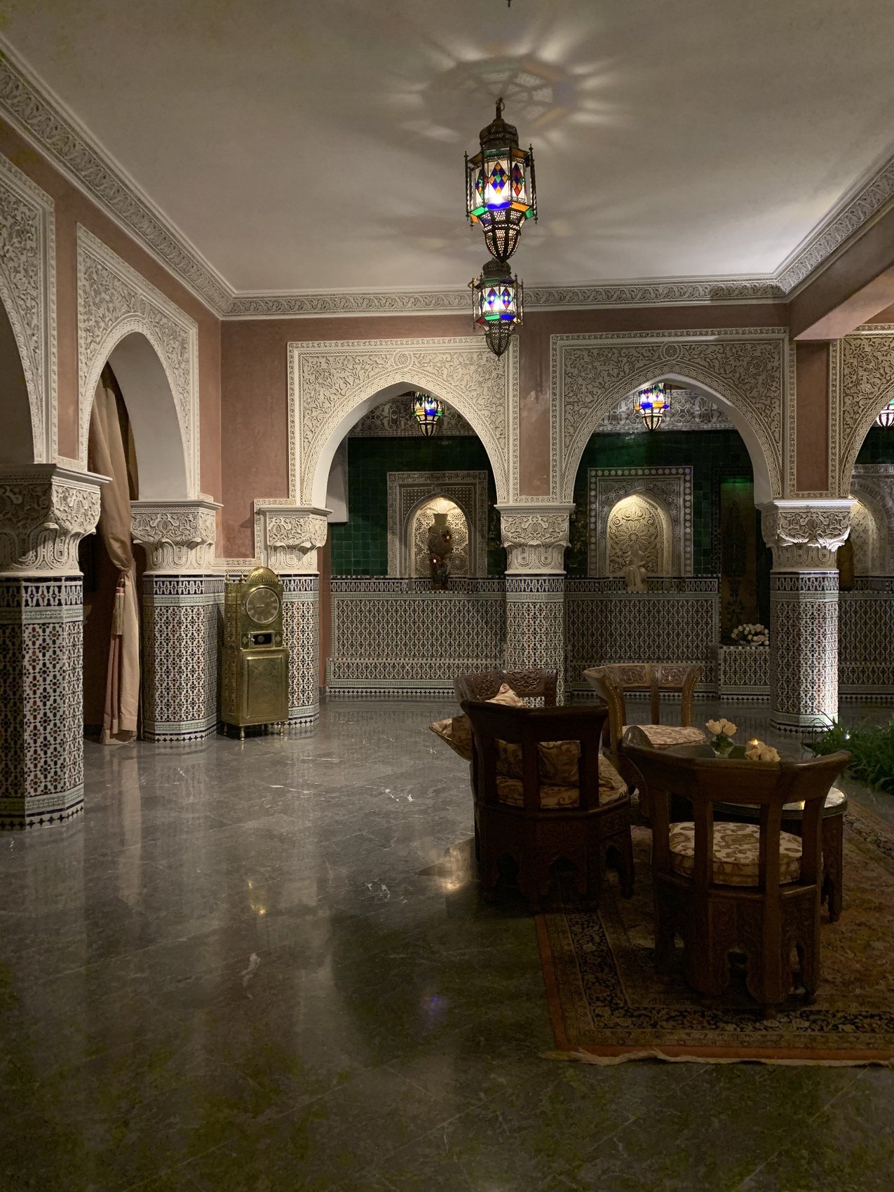 A salon at La Sultana at night with carved plaster arches, a hanging lantern and low tables on a patterned floor
