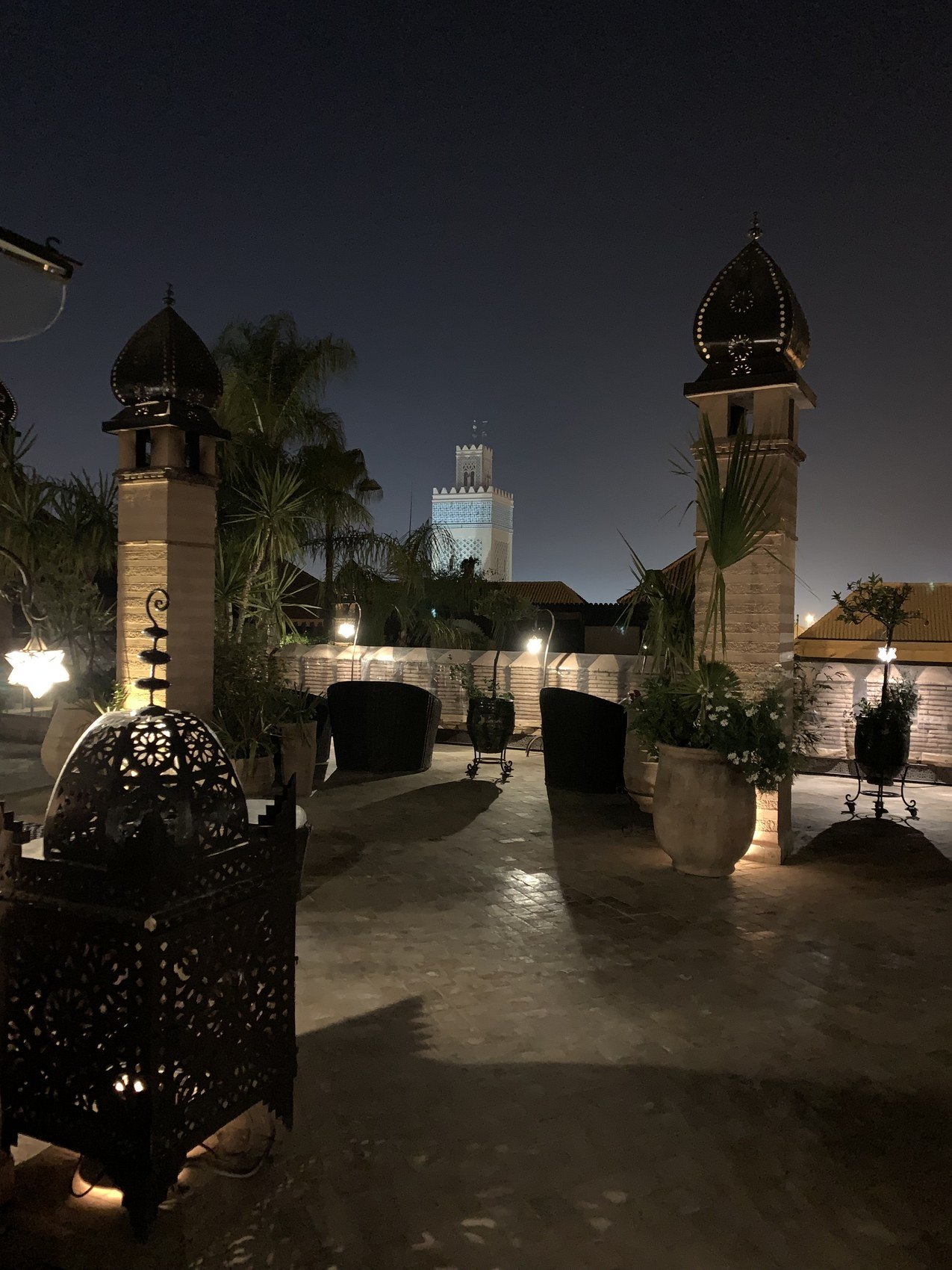 The Koutoubia minaret lit at night beyond the dark roof terrace at La Sultana with a pierced lantern in the foreground