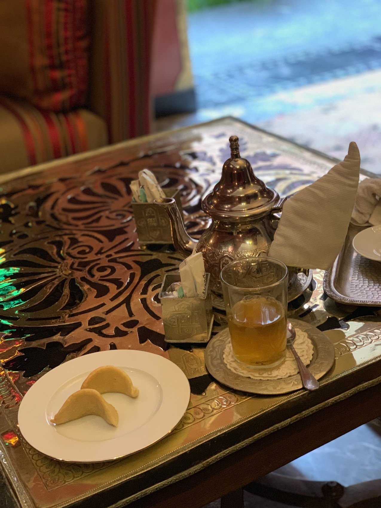 A brass teapot, a glass of mint tea and two crescent pastries on a carved table at La Sultana