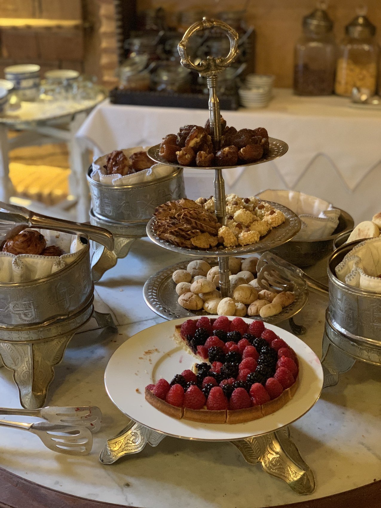 A tiered silver stand of Moroccan pastries and a berry tart on a laid table at La Sultana