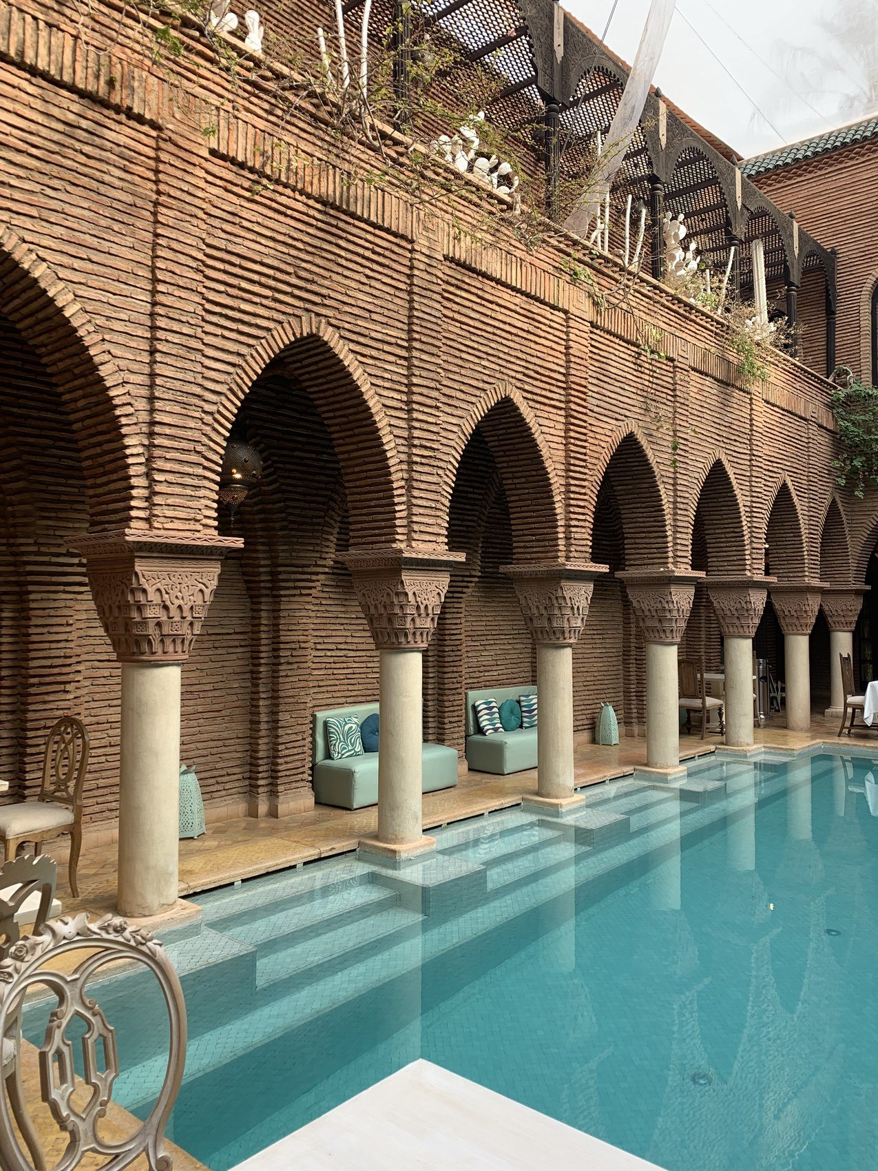 The pool at La Sultana in daylight between brick arcades with turquoise cushions on the stone benches