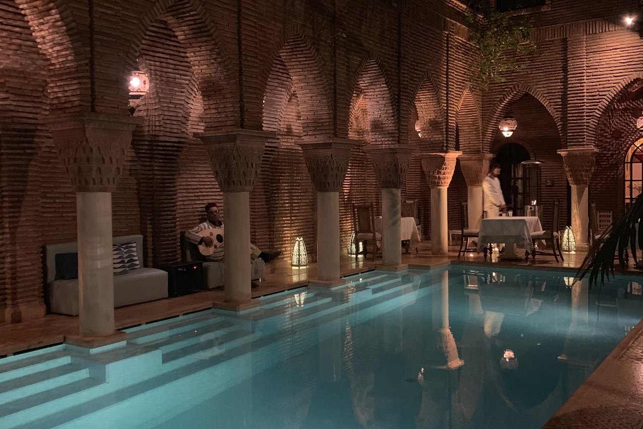 The pool at La Sultana lit at night between the brick arcades, with the arches reflected in the water