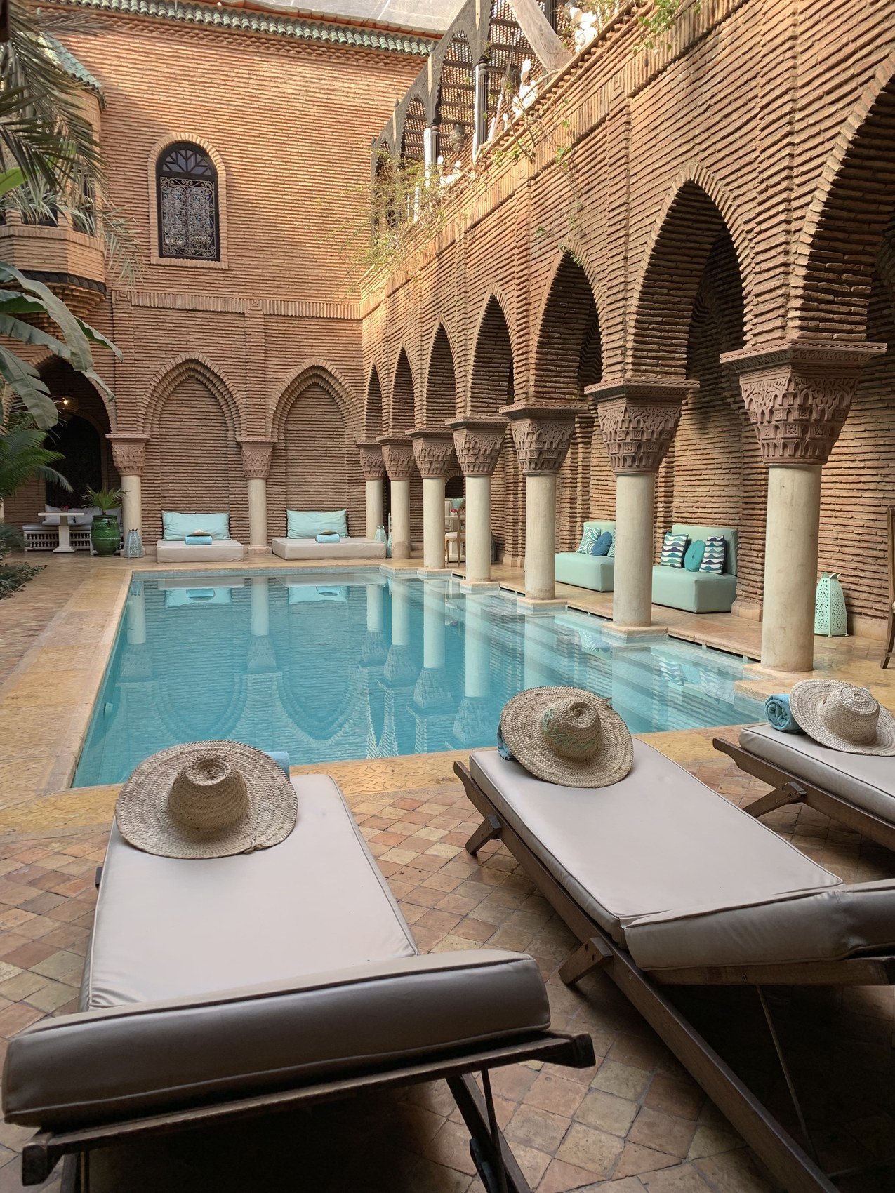 Two straw hats laid on loungers beside the pool at La Sultana with the brick arcade behind